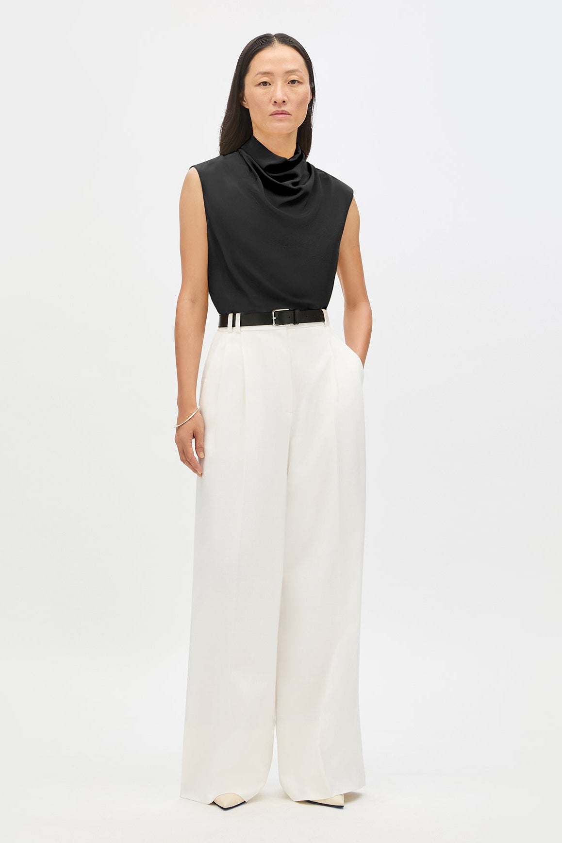 Woman wearing a black sleeveless top and white pants on a white background