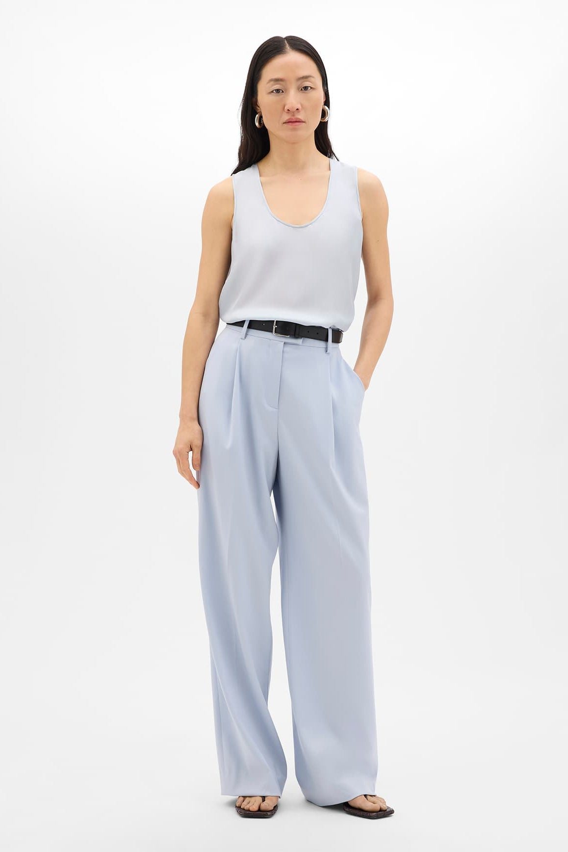 Woman wearing a light gray sleeveless top and light blue wide-leg pants on a white background