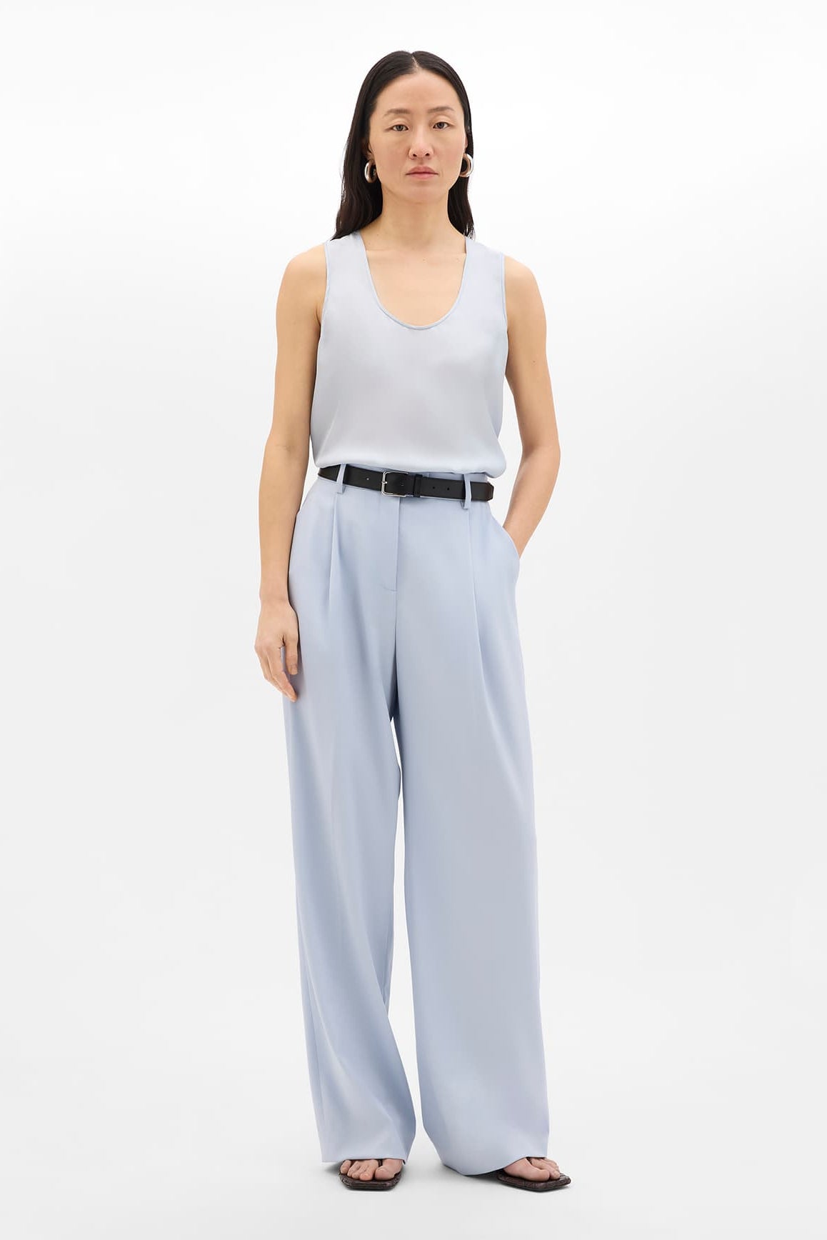 Woman wearing a white sleeveless top and light blue wide-leg pants on a white background