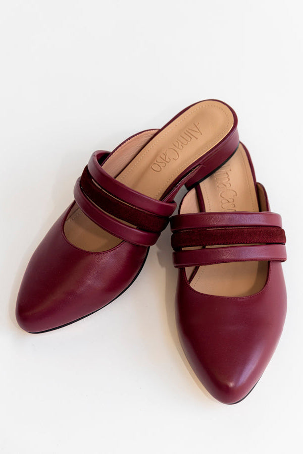 A pair of burgundy pointed-toe mule heels with double strap detailing, shown from a top-down angle on a white background.
