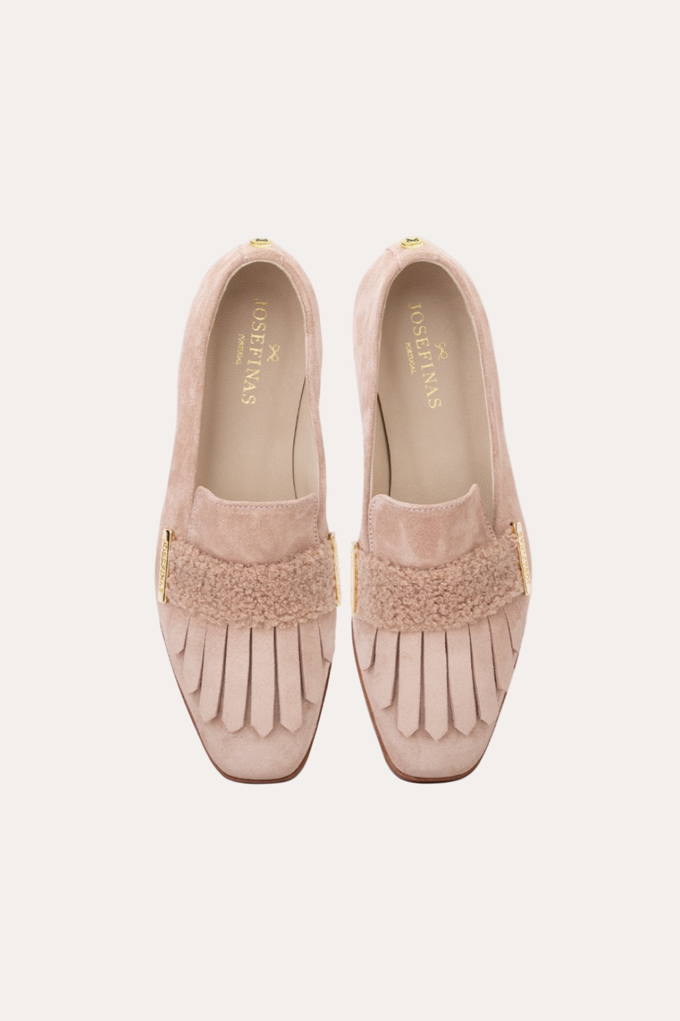Pair of pink loafers with fringe details on a light beige background