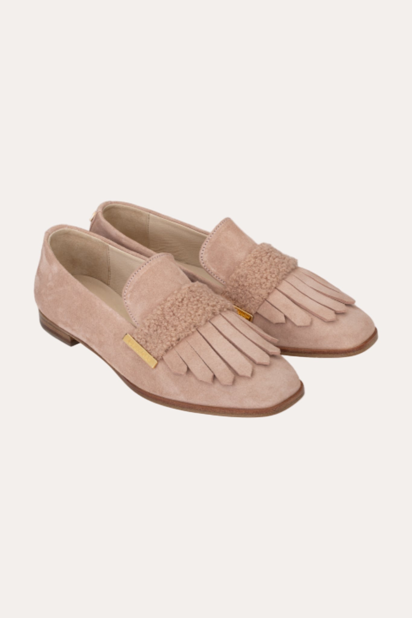 Pair of beige loafers with fringes on a light beige background