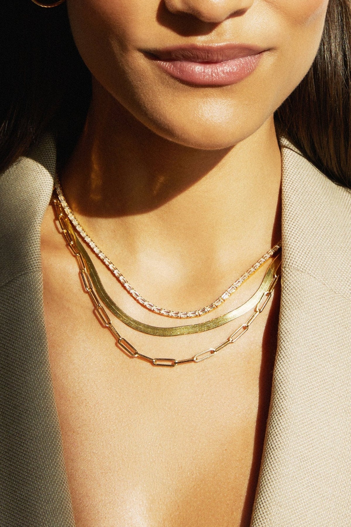 Close-up of a woman wearing multiple gold necklaces against a neutral background