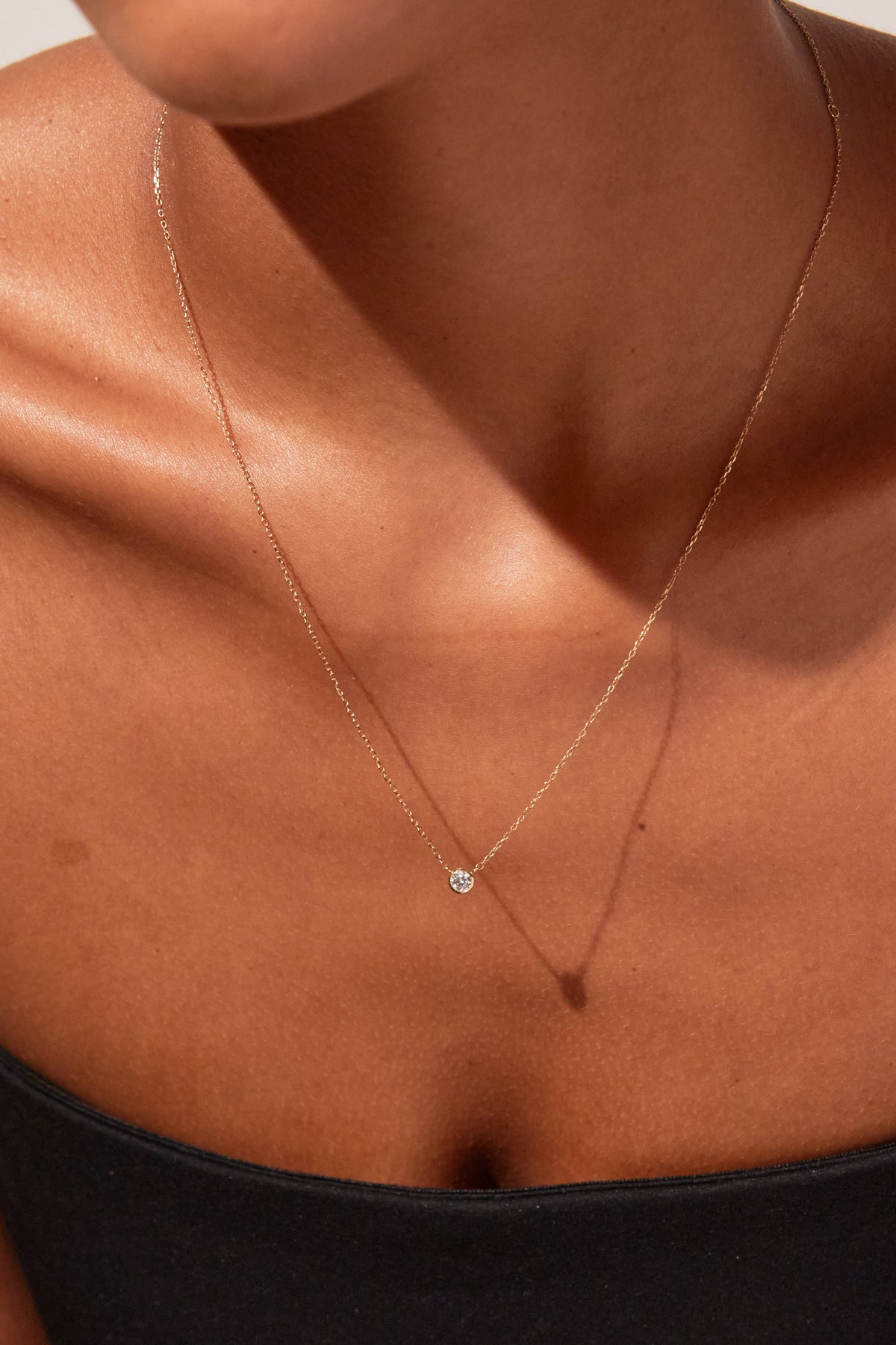 Necklace with a small pendant on a person wearing a black top against a neutral background
