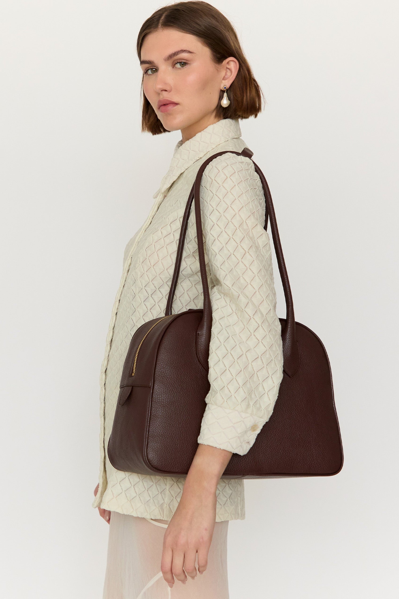 Woman holding a brown leather handbag against a white background