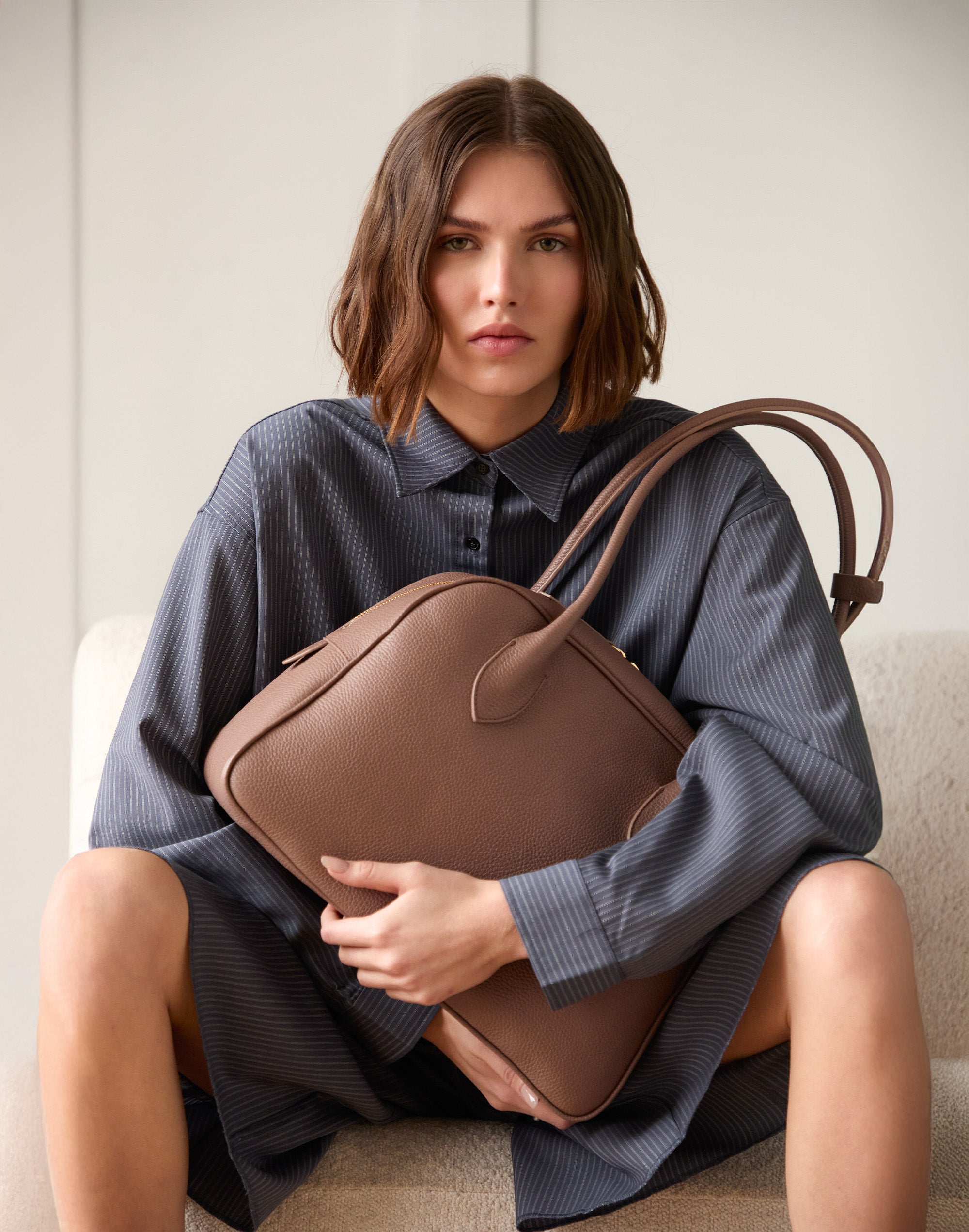 Woman holding a brown handbag against a neutral background