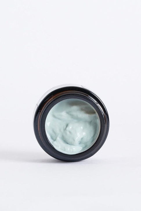 Small jar of light green cream on a white background