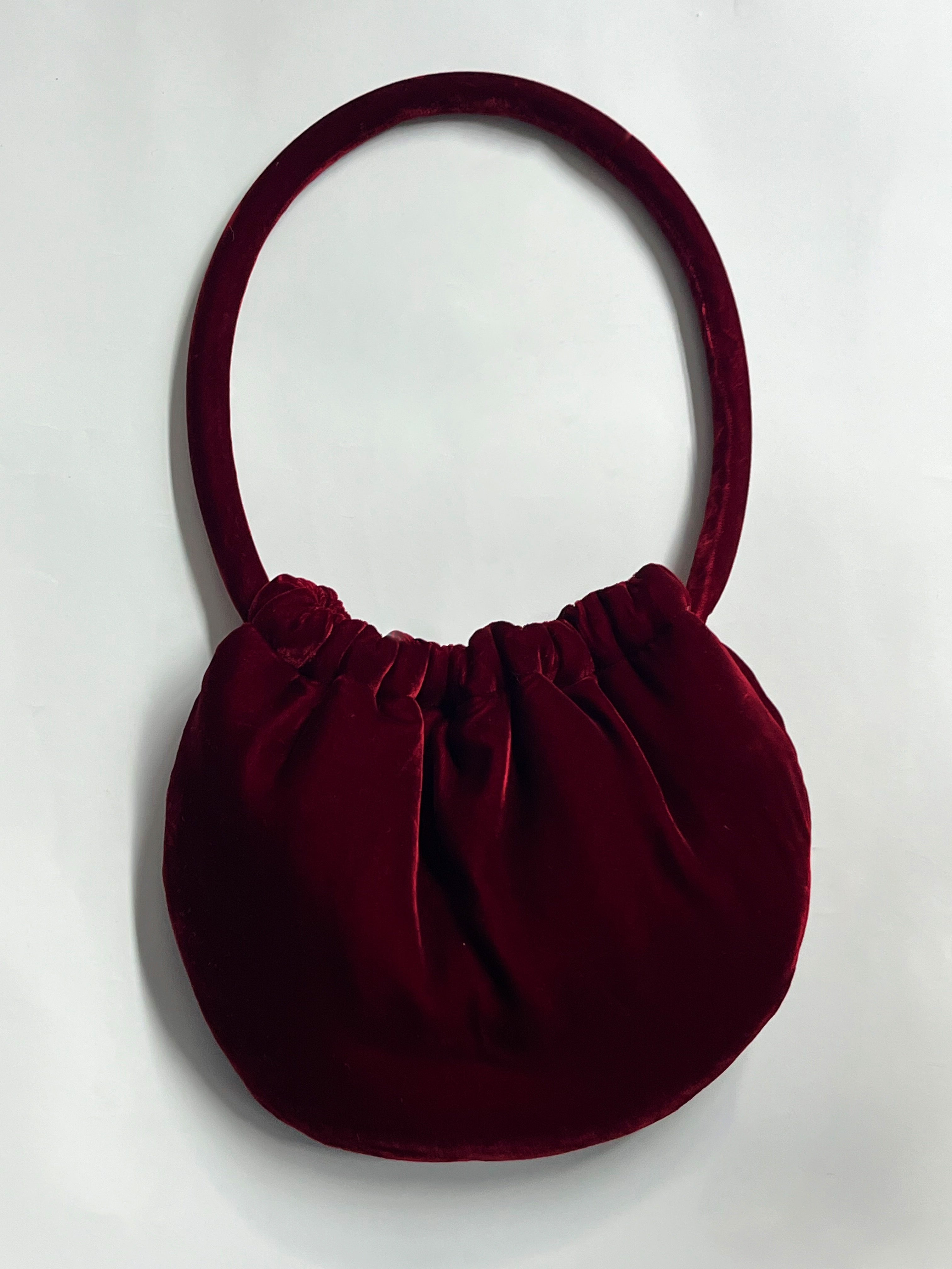 Maroon handbag with a round shape and handle on a white background