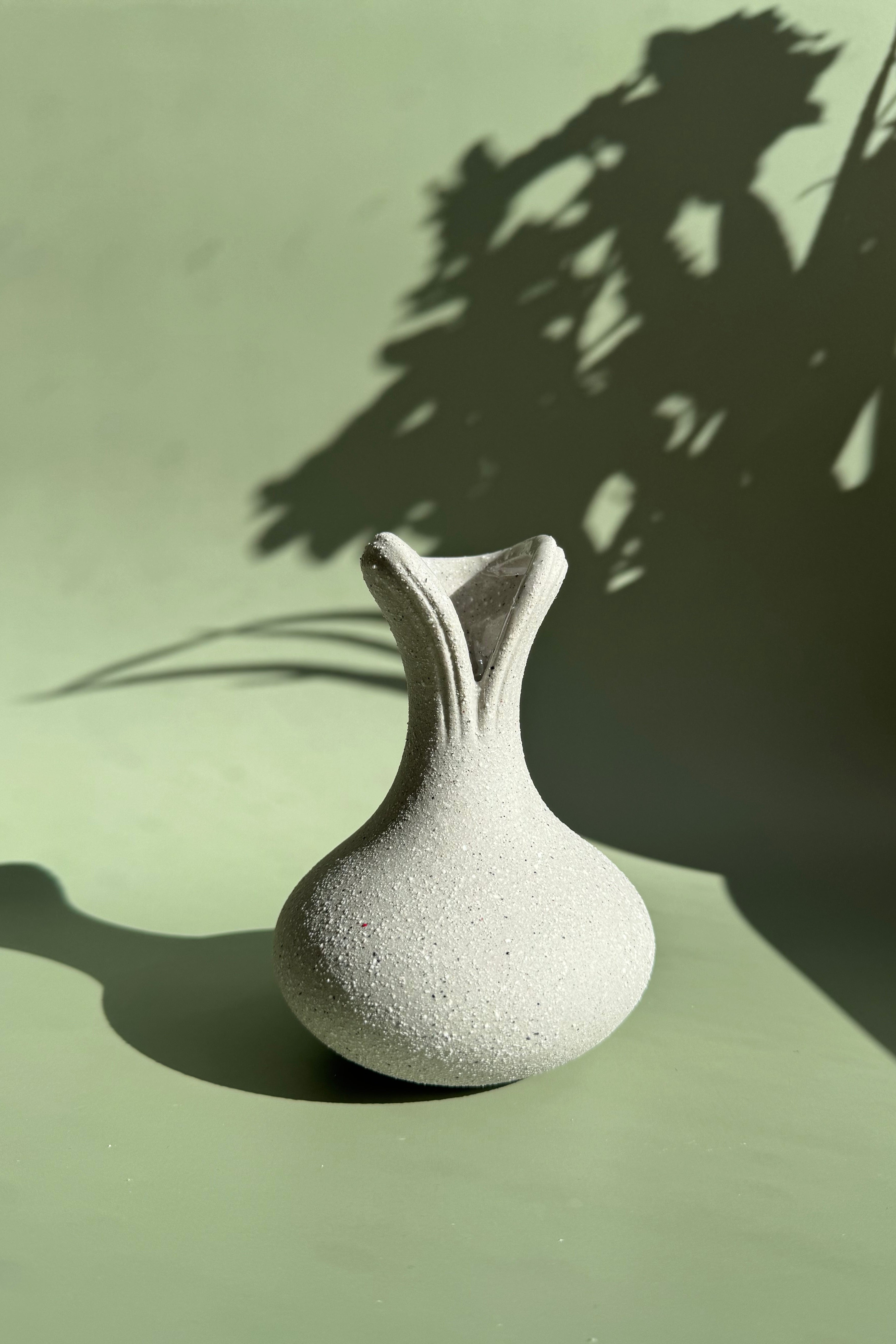 White textured vase on a light green surface with plant shadows