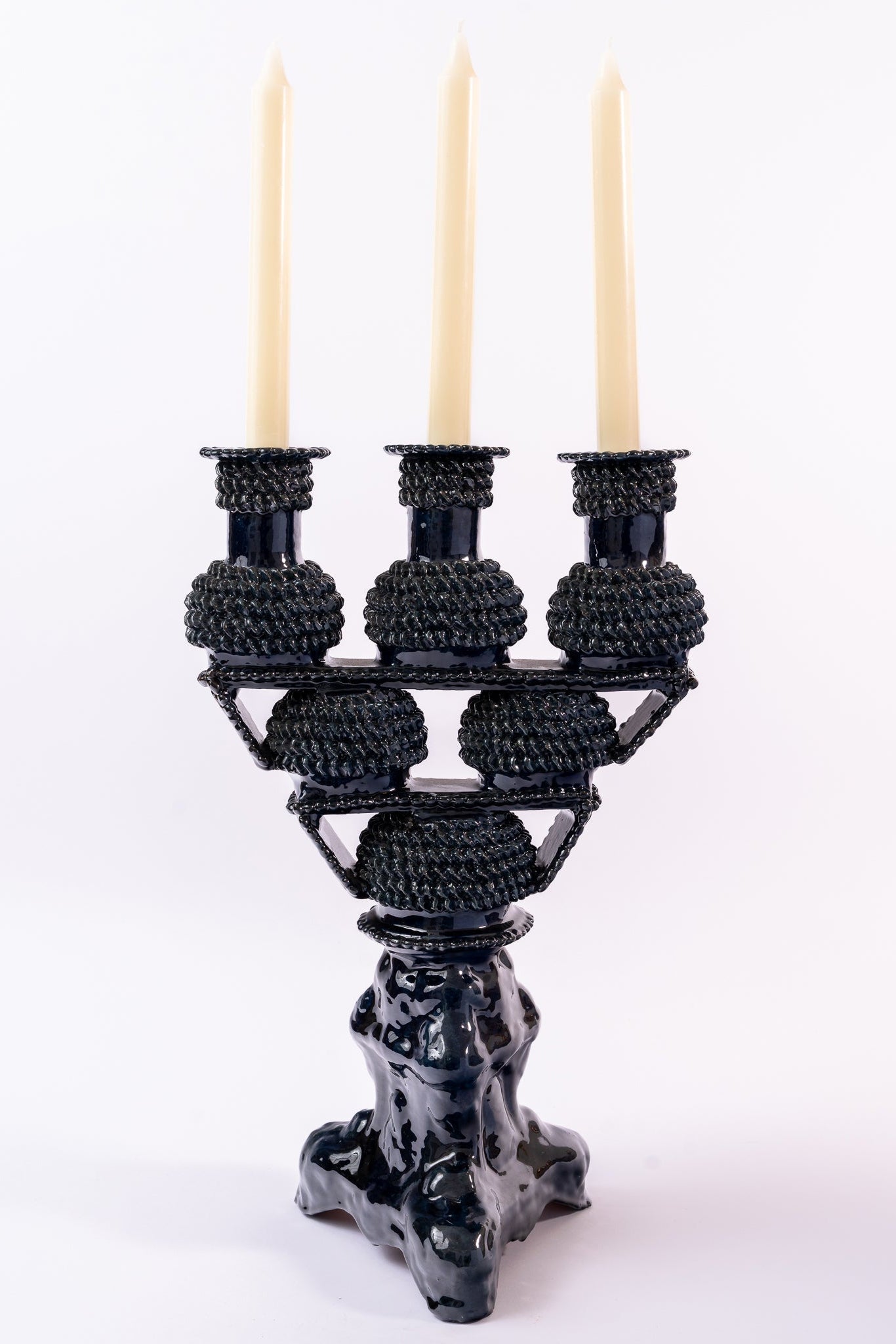 Black candle holder with three lit candles on a white background