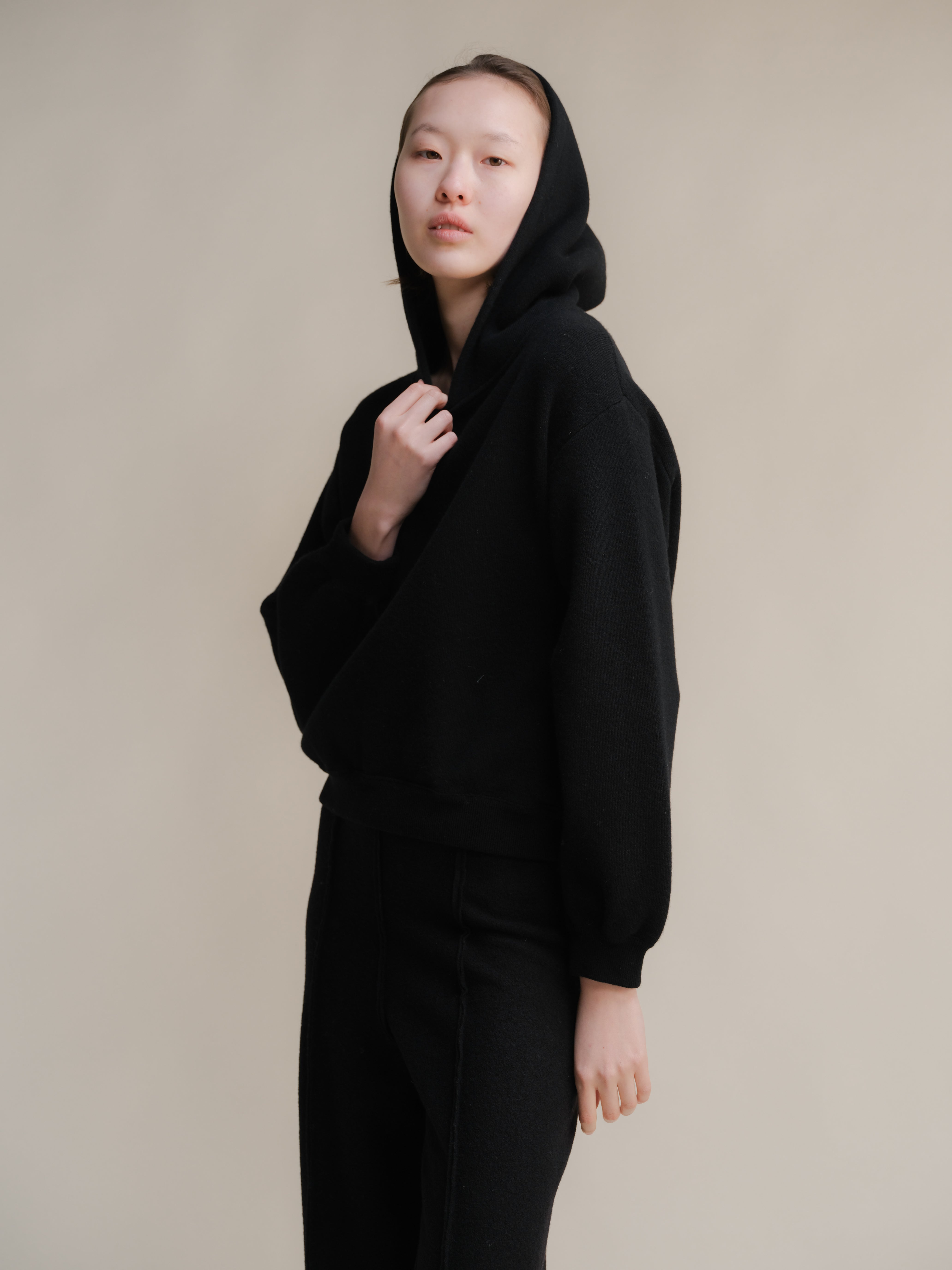 Person wearing a black hooded outfit against a plain background