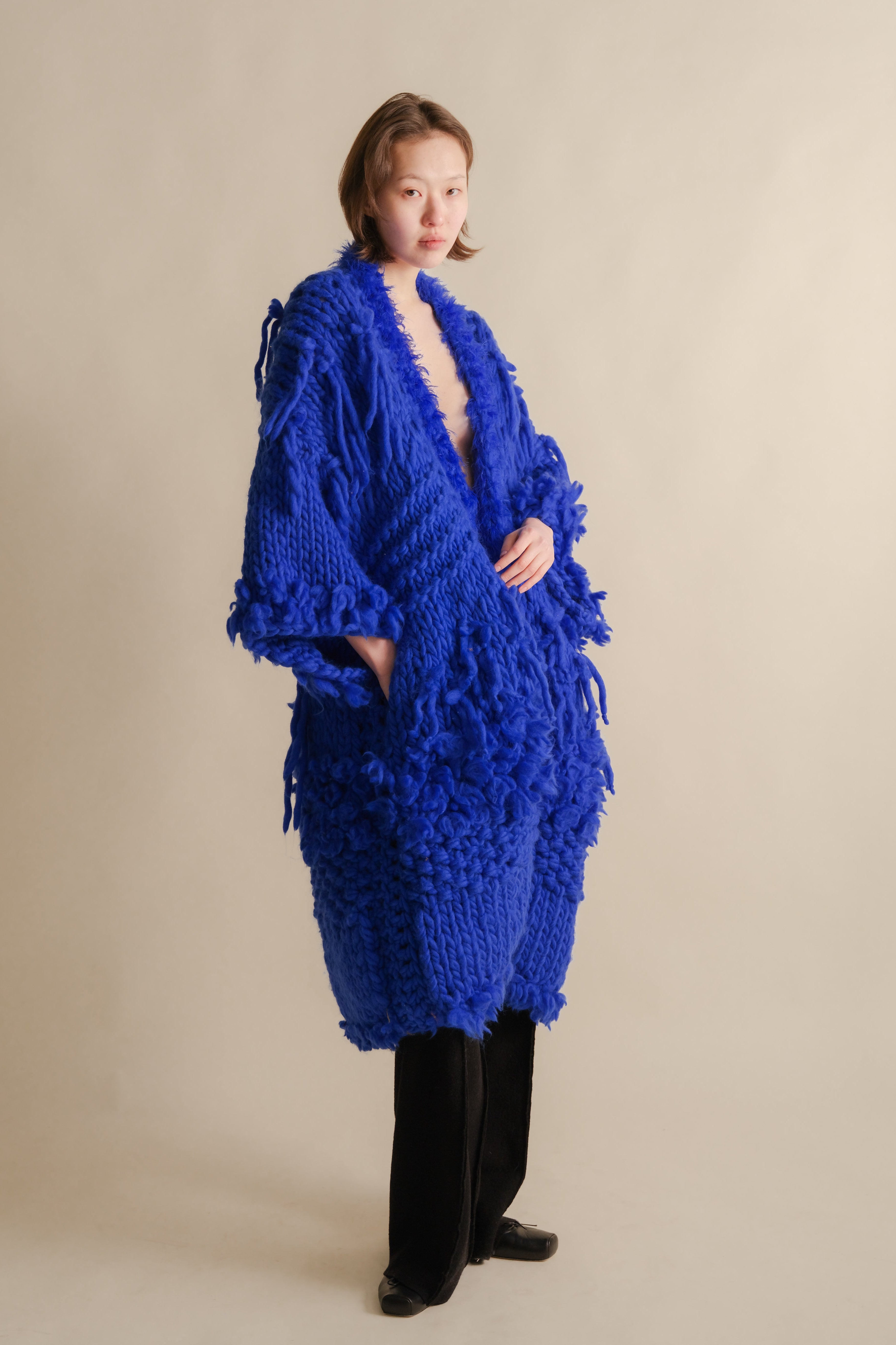 Person wearing a blue knitted cardigan on a beige background