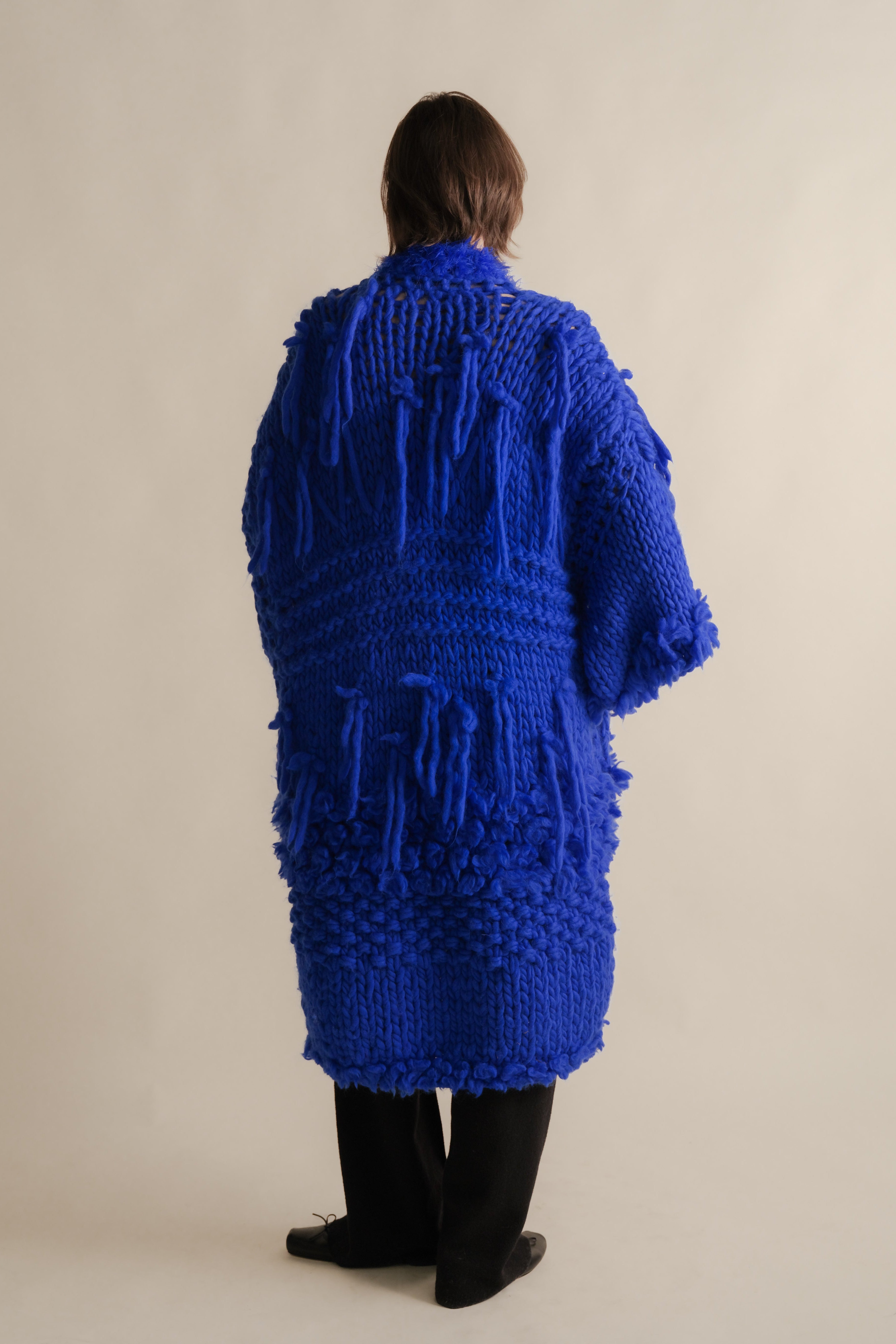 Person wearing a blue knitted cardigan on a beige background