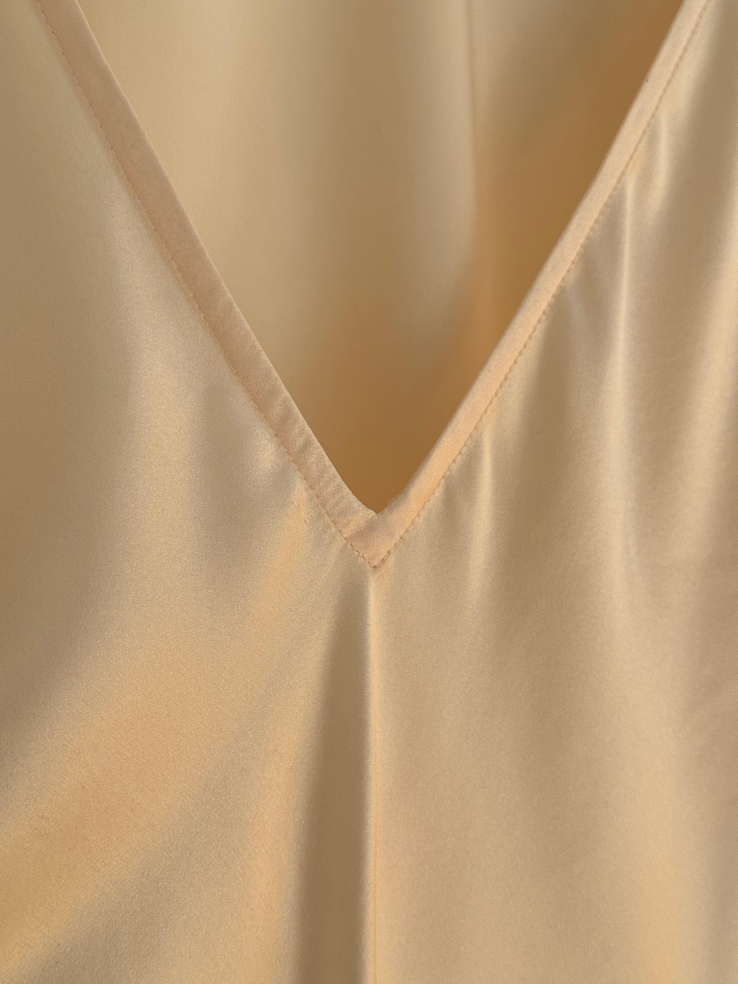 Close-up of a cream-colored silk satin fabric with a V-neckline and soft draped folds.