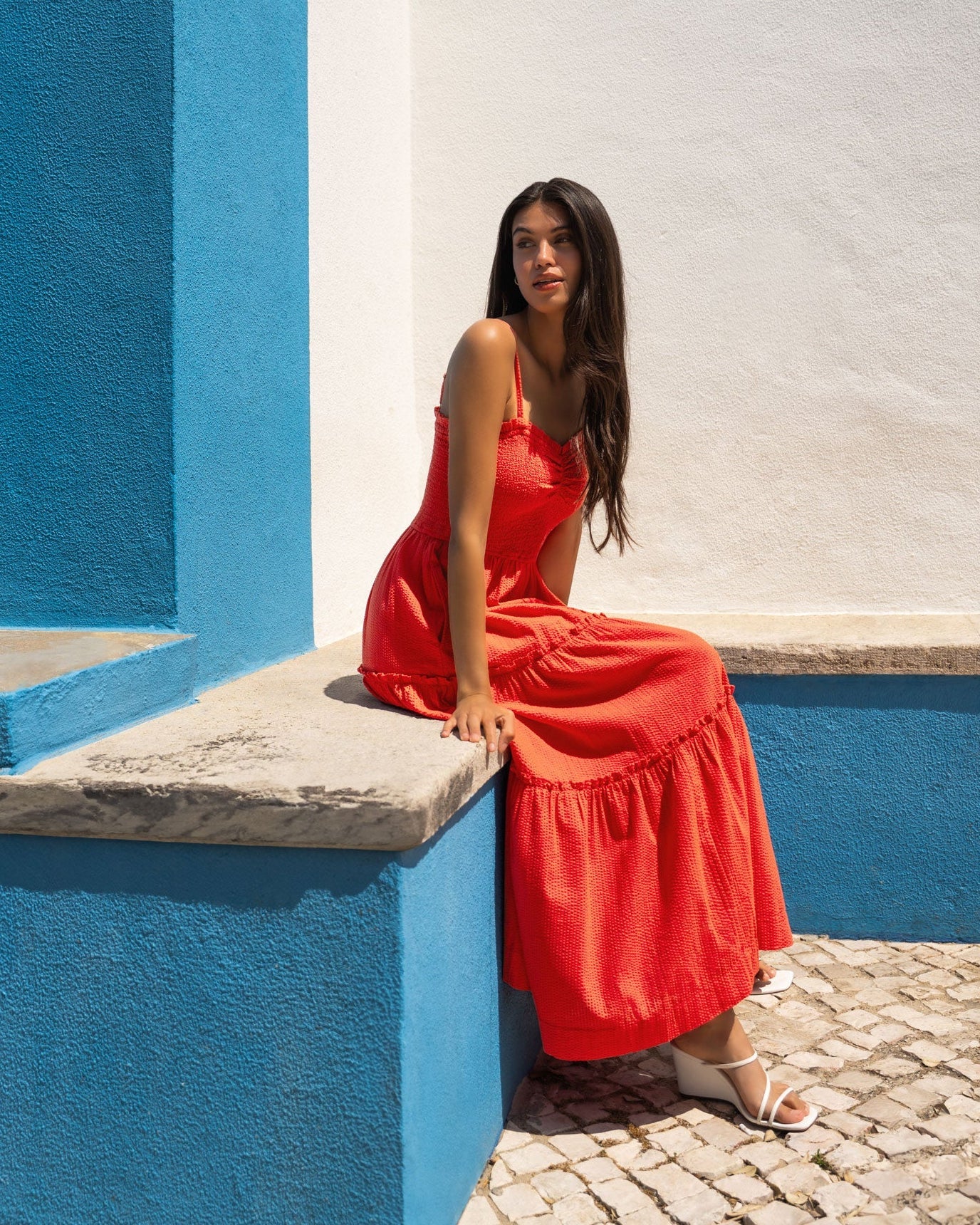 Woman in a red dress sitting on a blue and white wall.