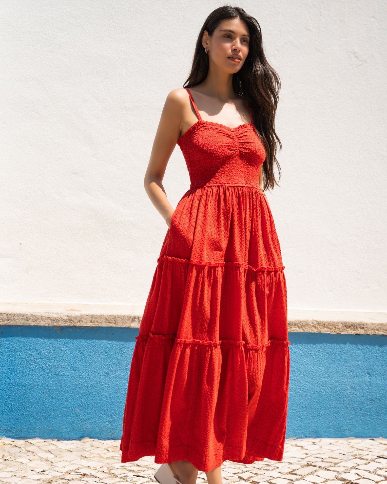 Woman wearing a red dress standing against a white wall with a blue base.