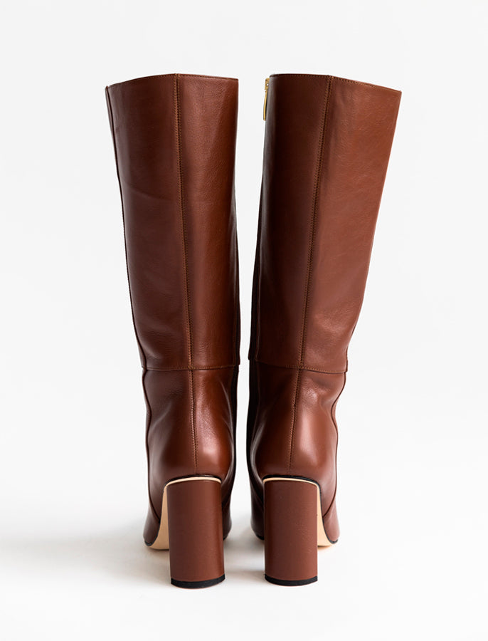 A pair of brown leather knee-high boots with block heels, shown from the back against a plain white background.
