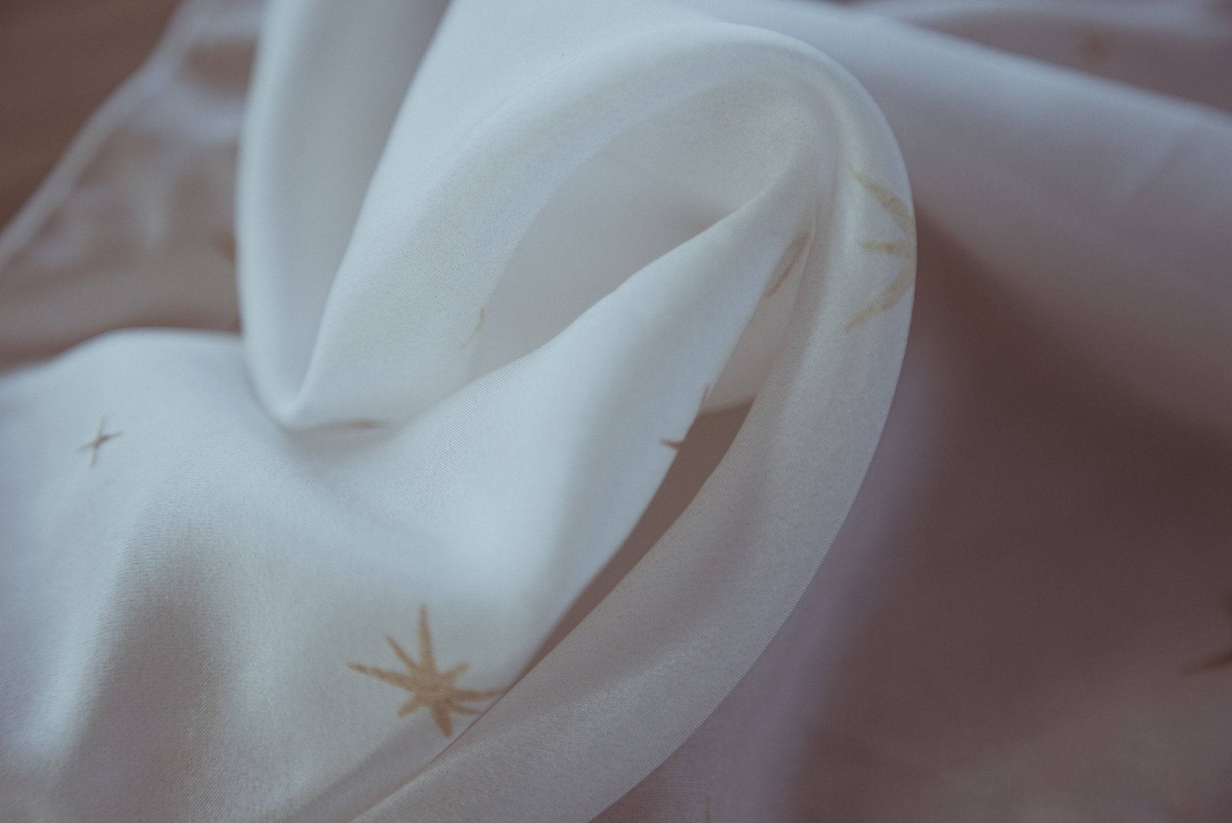 Close-up of white fabric with small gold star patterns on a soft pink background