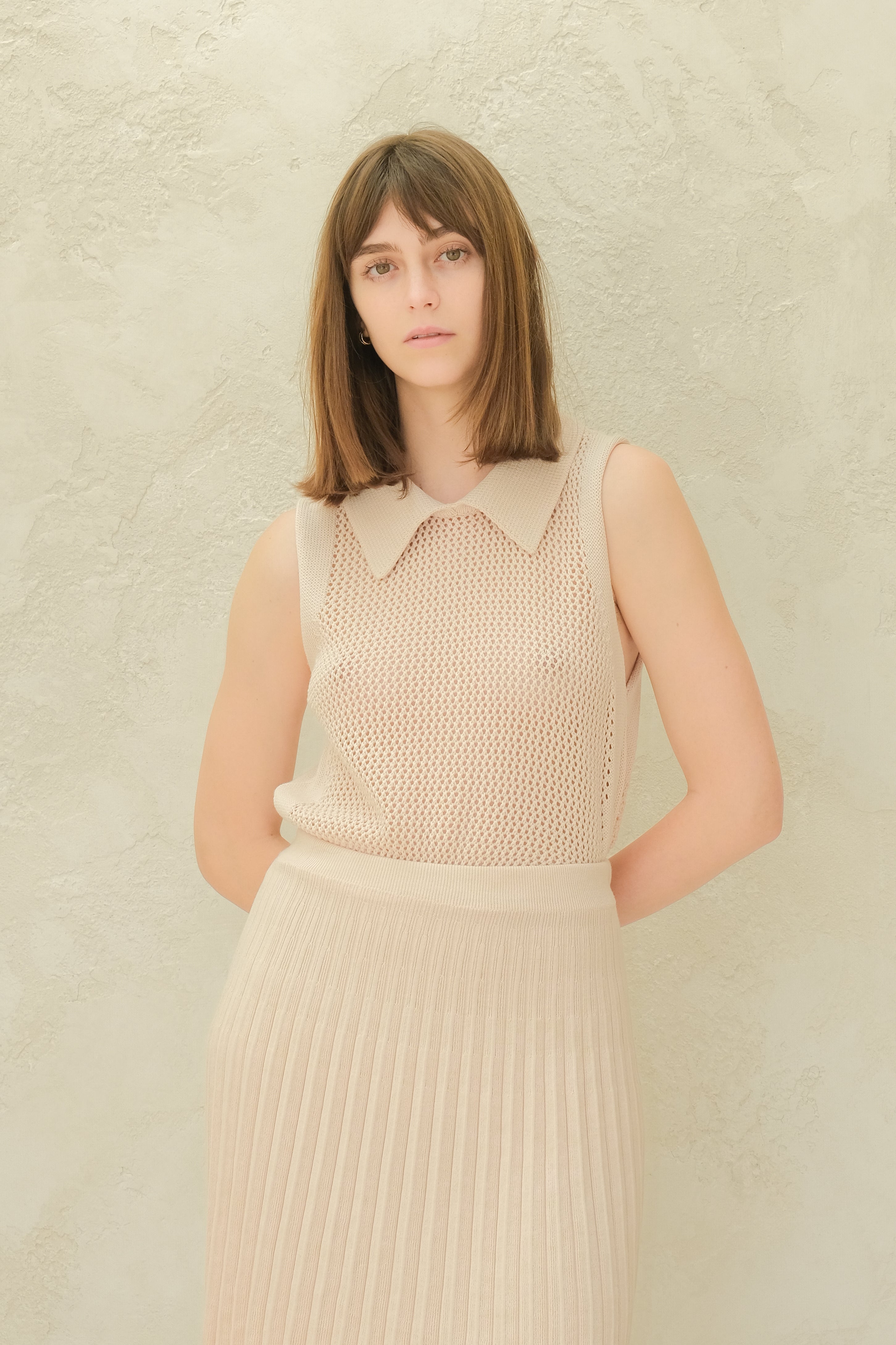 Woman wearing a beige sleeveless top and pleated skirt against a light background