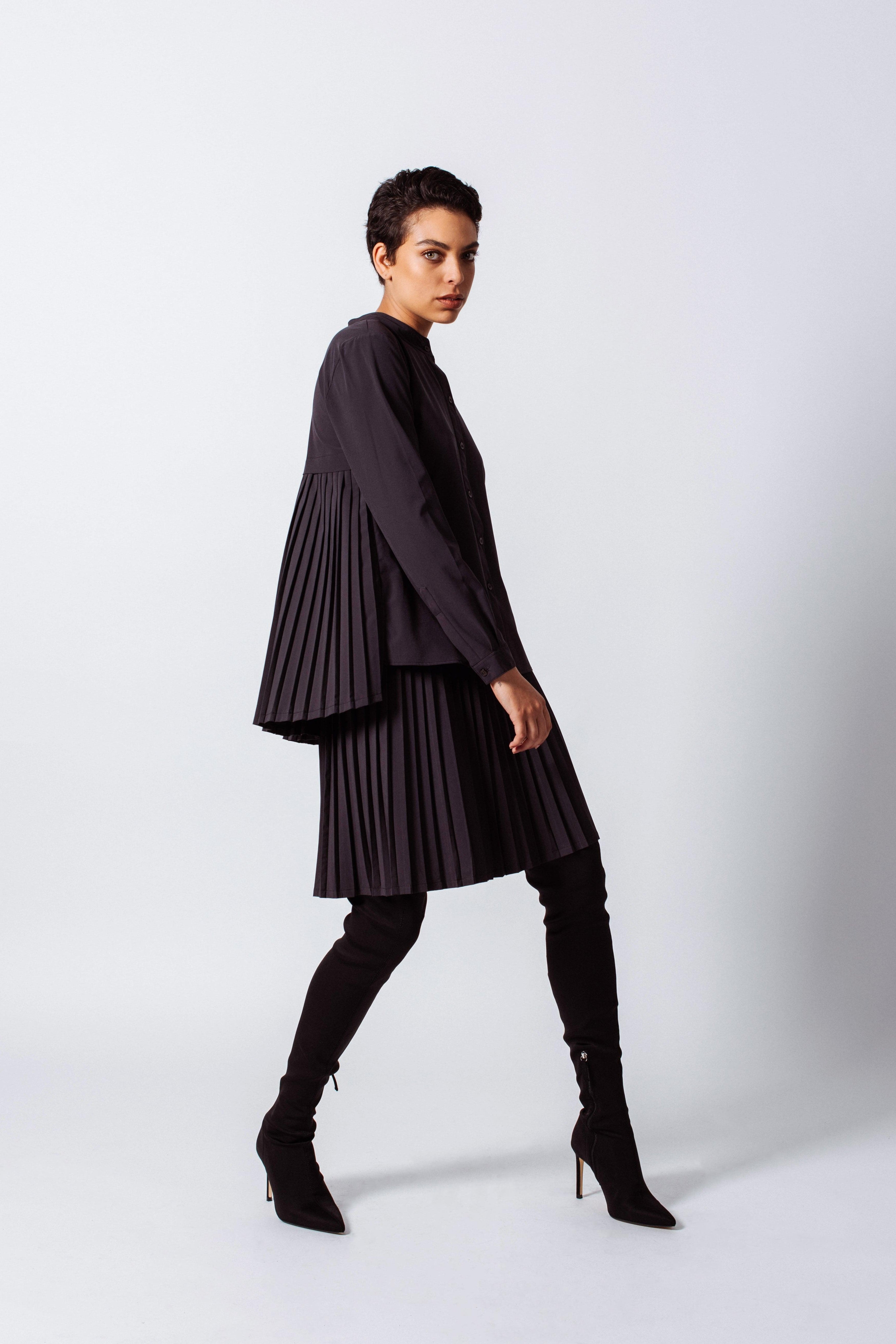 Person wearing a black pleated outfit with high-heeled boots on a white background