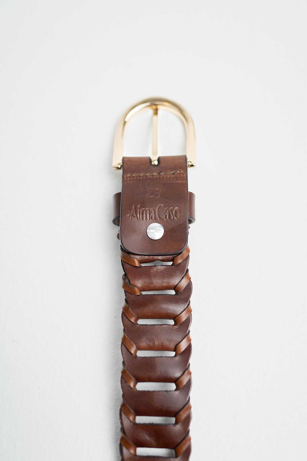 A close-up of a brown leather belt with a braided woven pattern, a gold-tone metal buckle, and a branded leather keeper embossed with 'Alfa Caso'.
