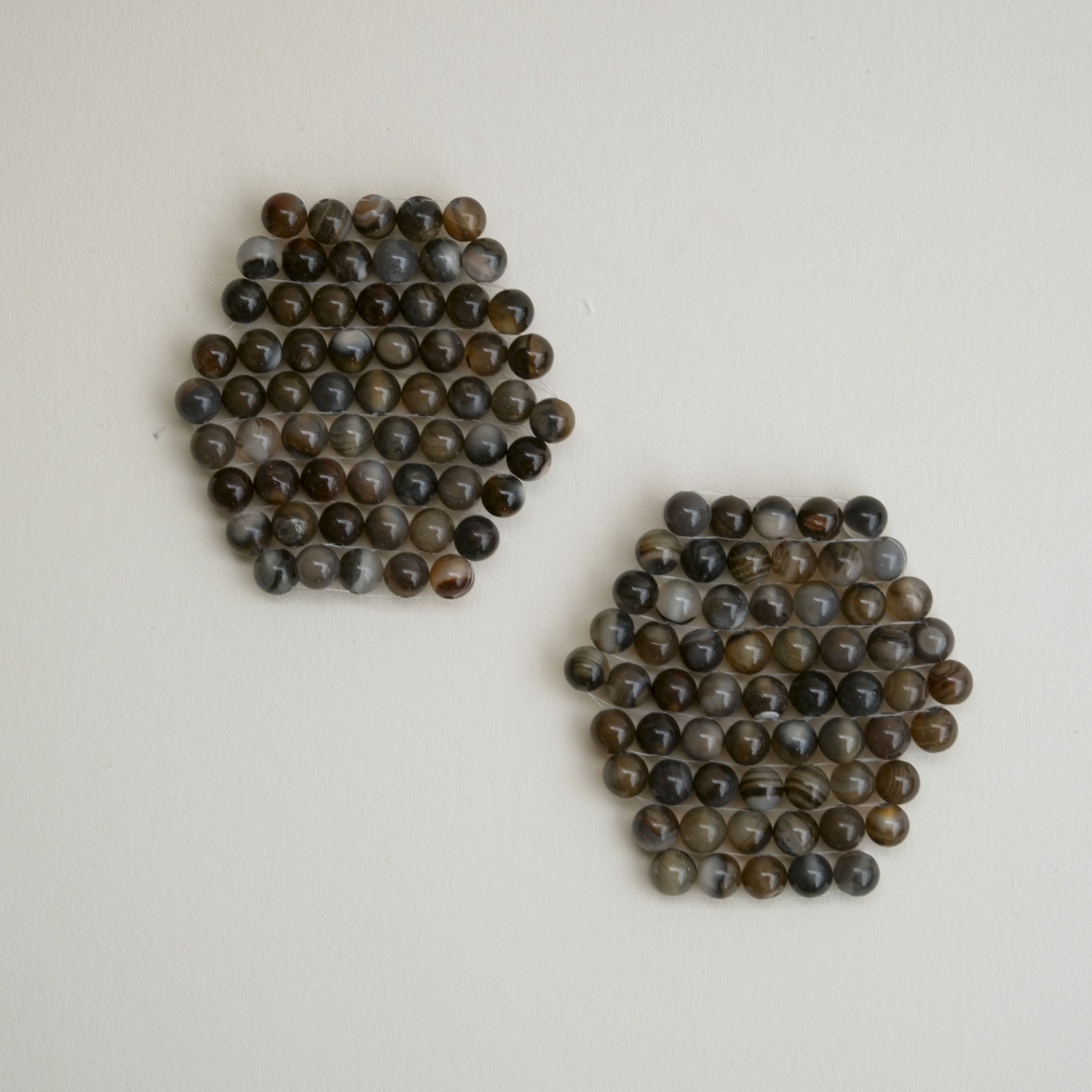 Two clusters of small round agate beads in earthy brown, gray, and black colors, arranged on a plain off-white background.