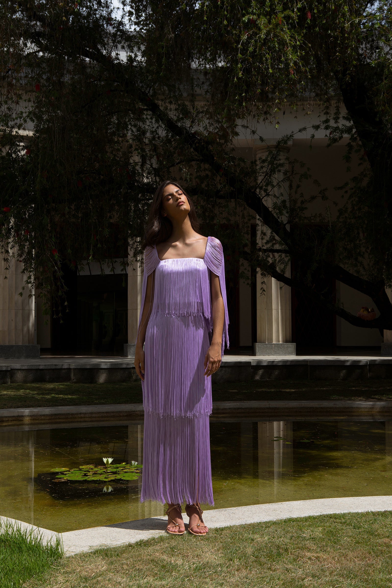 Woman in a purple dress standing by a pool with trees in the background