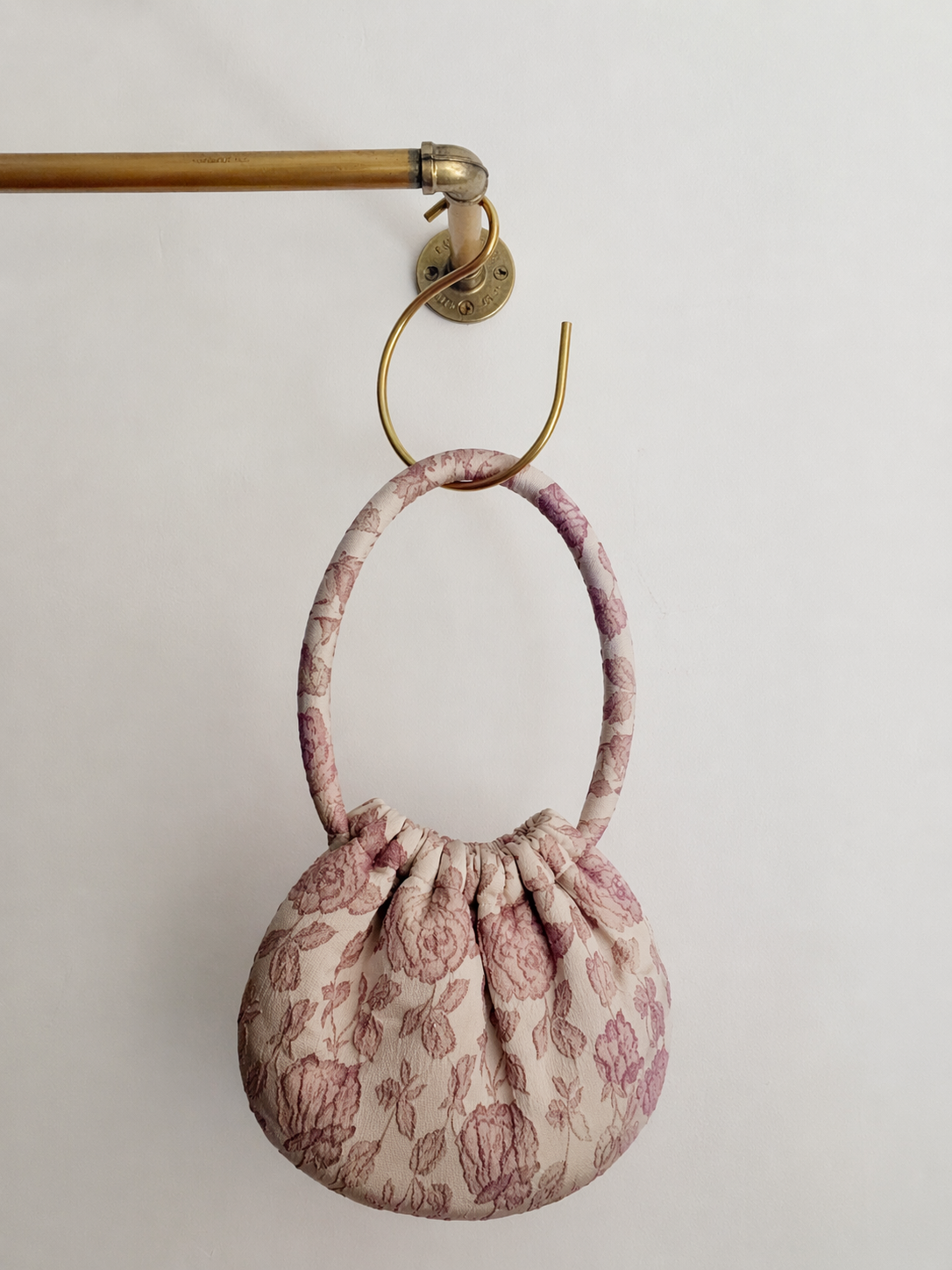 Small fabric pouch with floral pattern hanging on a brass hook against a light background