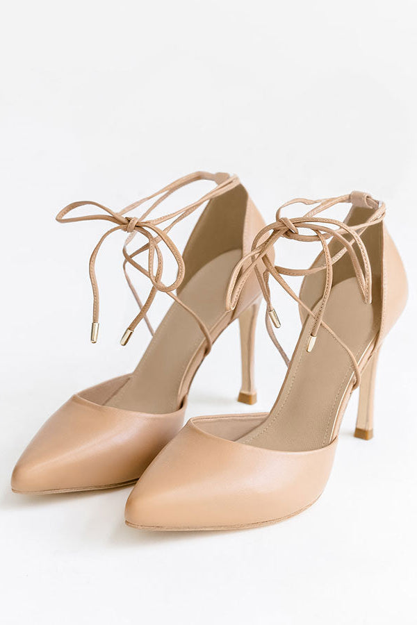 A pair of beige pointed-toe high heels with thin lace-up ankle straps, photographed on a clean white background.