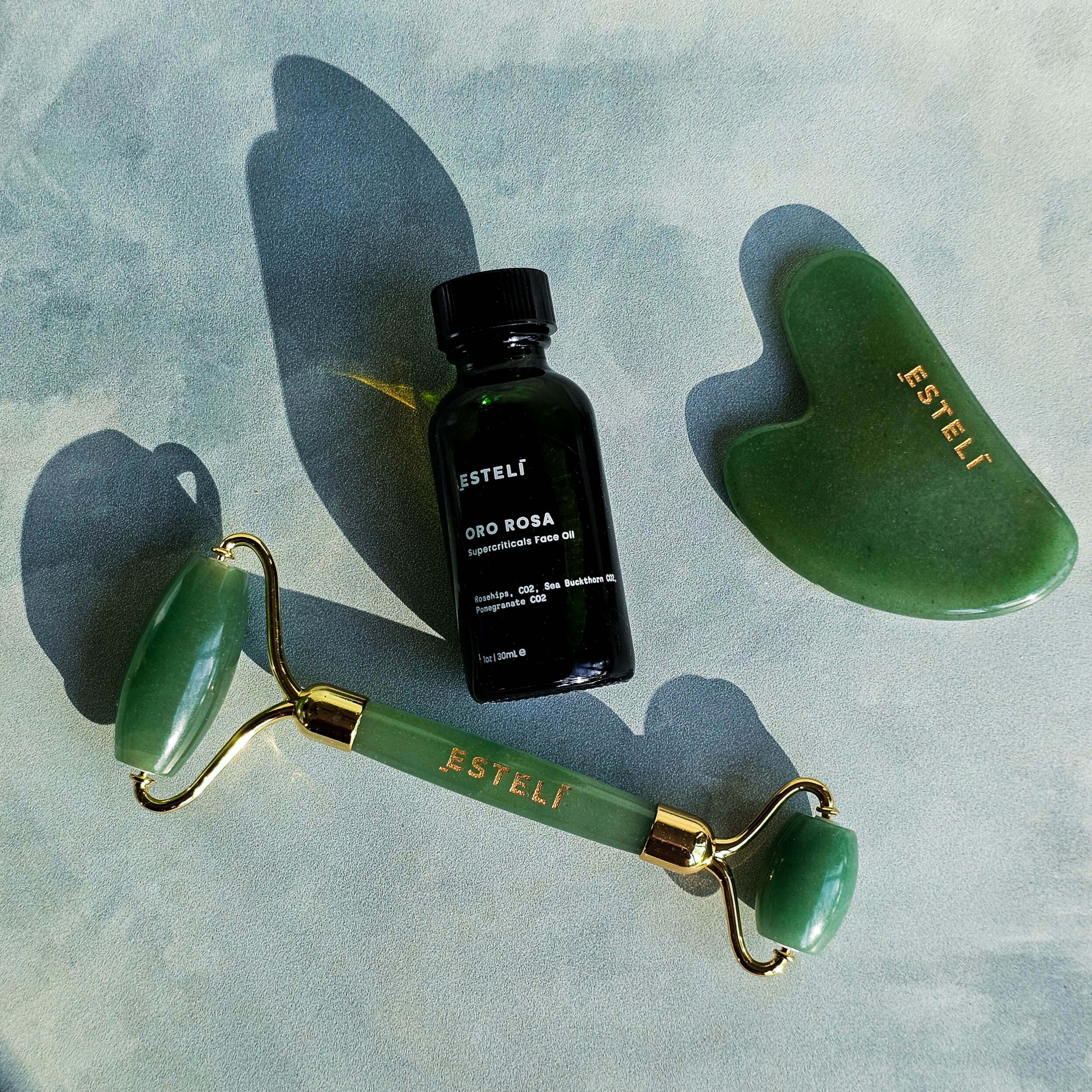 Esteli jade roller, bottle, and gua sha tool on a textured surface
