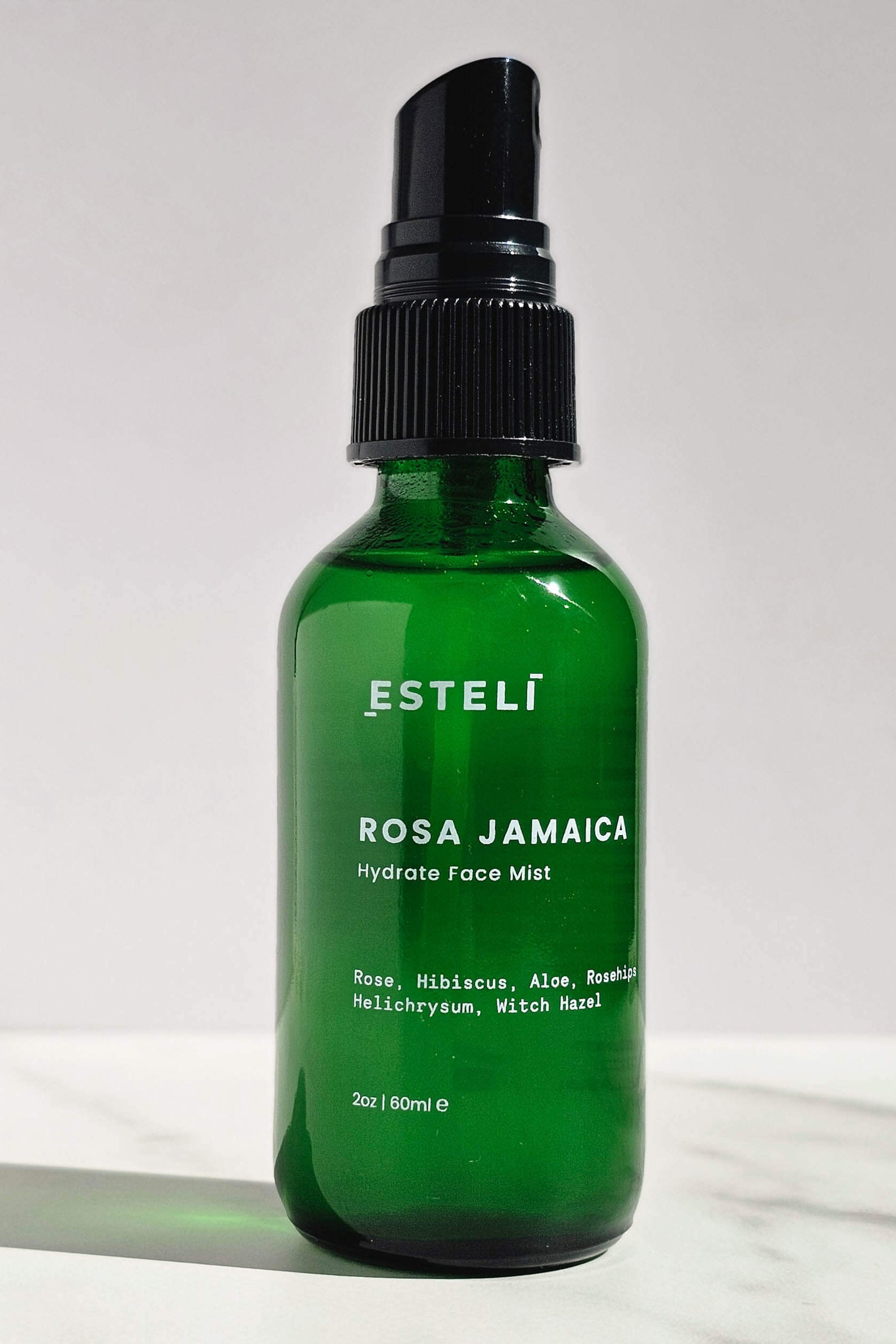 Green bottle of Estéli Rosa Jamaica Hydrate Face Mist on a white background