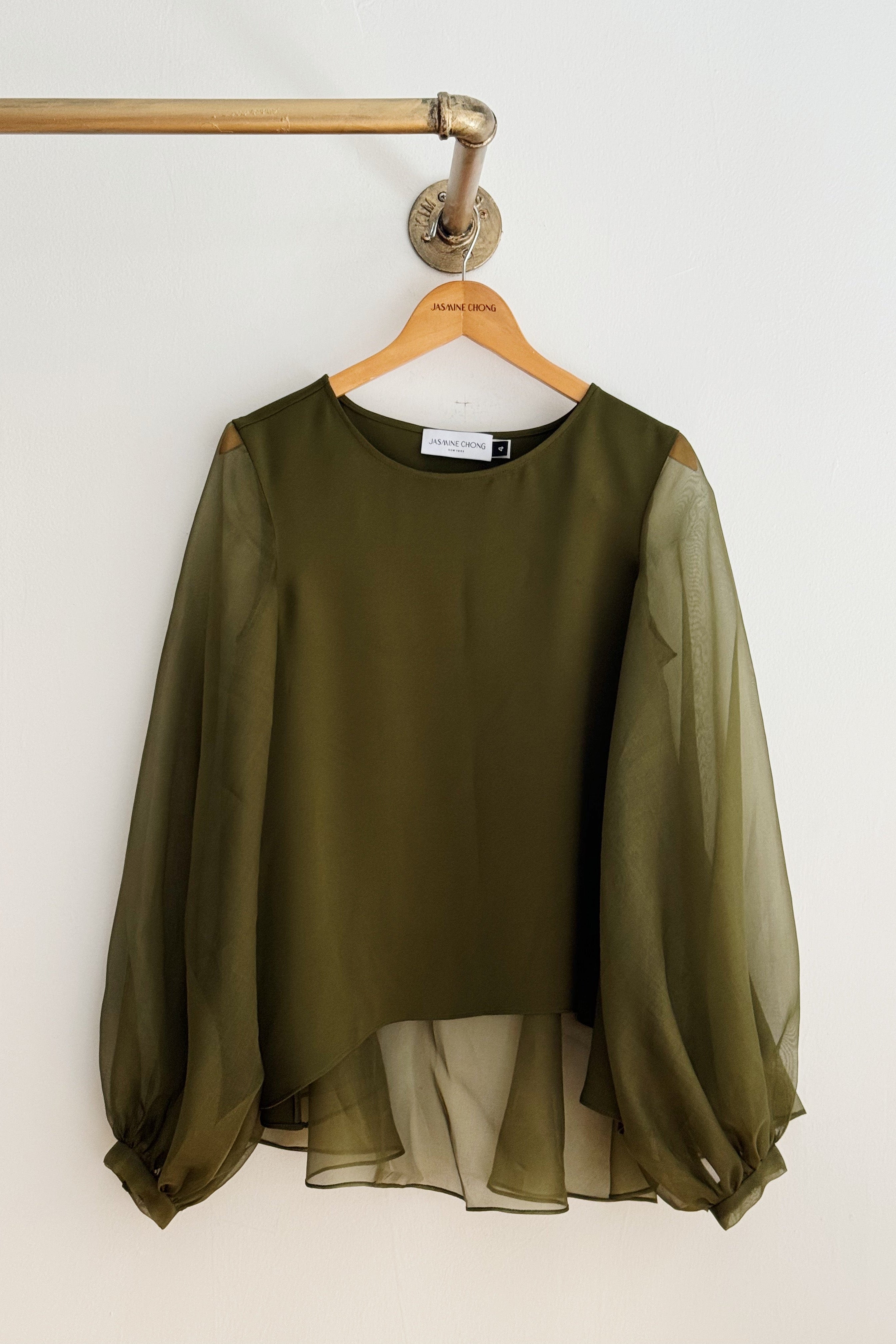 Green blouse with sheer sleeves on a wooden hanger against a white wall