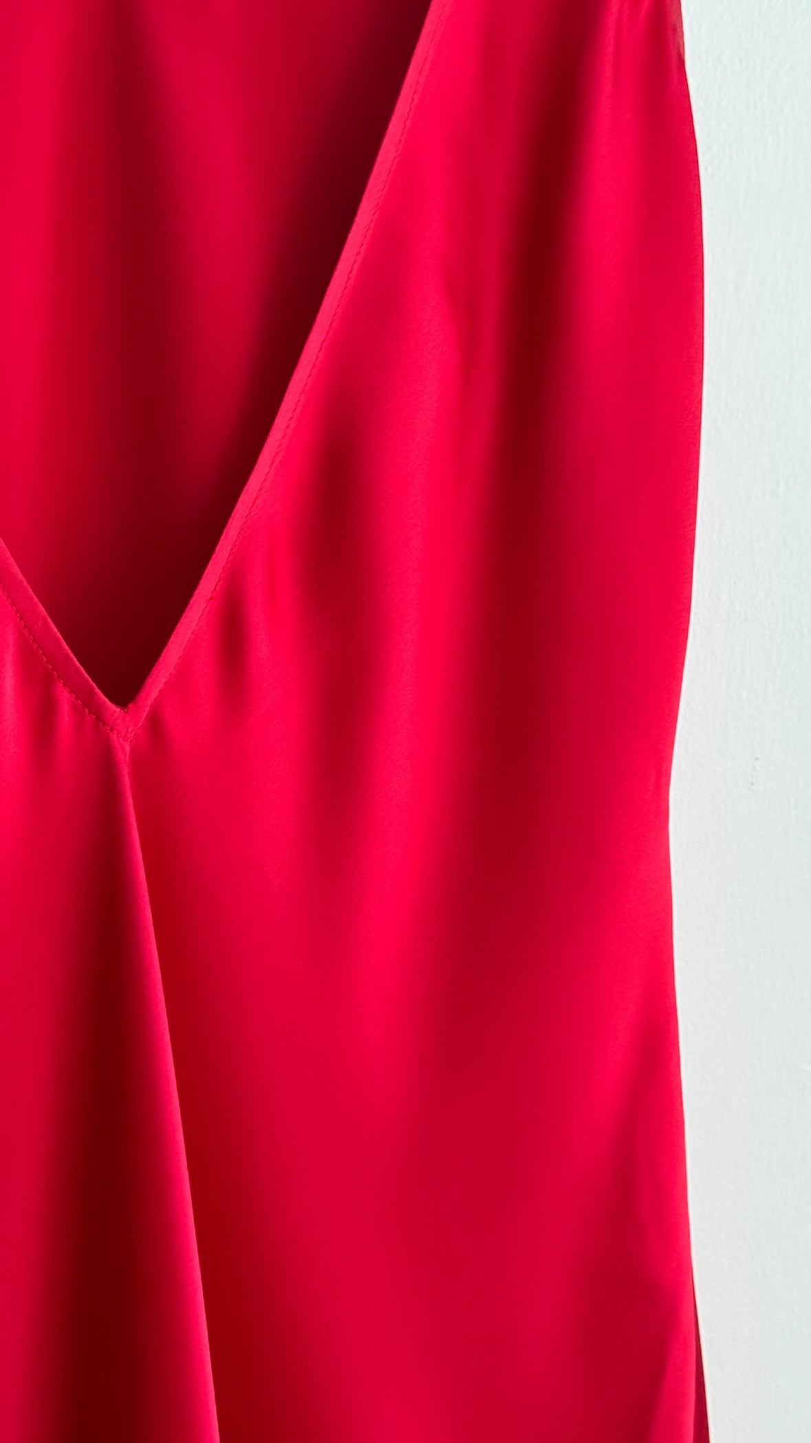 A close-up of a bright red satin silk fabric with a deep V-neckline, showing soft folds and a light gray background on the right side.