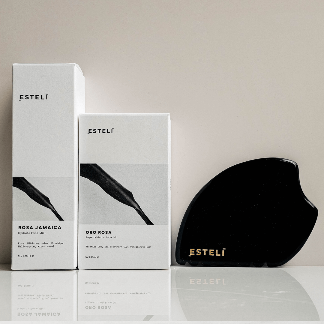 Two Esteli boxes and a black obsidian gua sha on a reflective surface with a neutral background