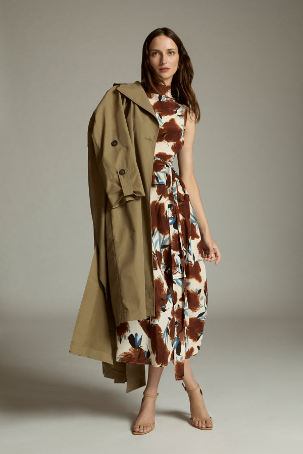 Woman wearing a floral dress with a long green coat against a neutral background | Exclude