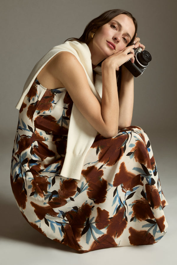 Woman in a floral dress holding a camera against a neutral background | Exclude | ALT GRID