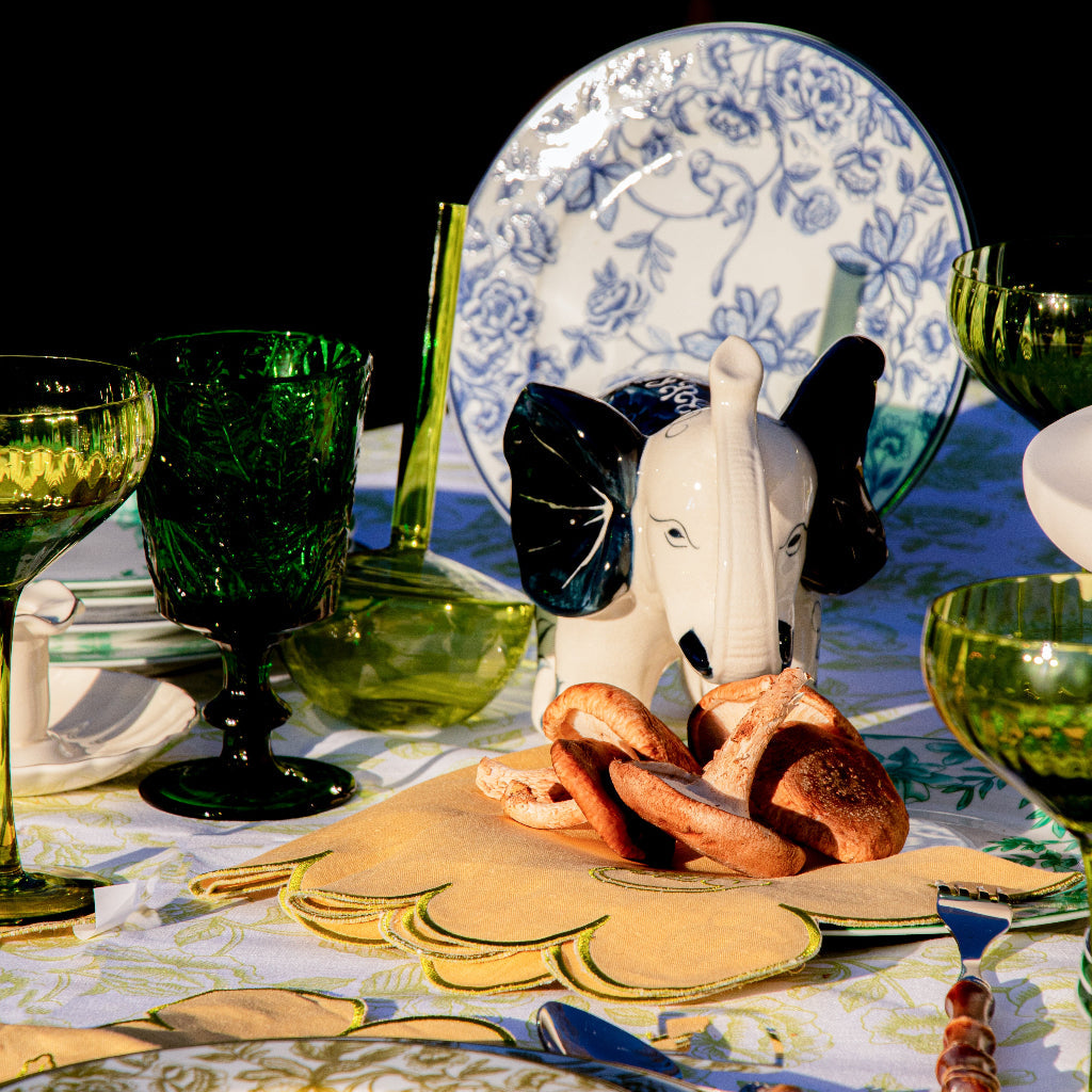 Dinner table setting with floral plates, green glasses, and a decorative elephant figurine.