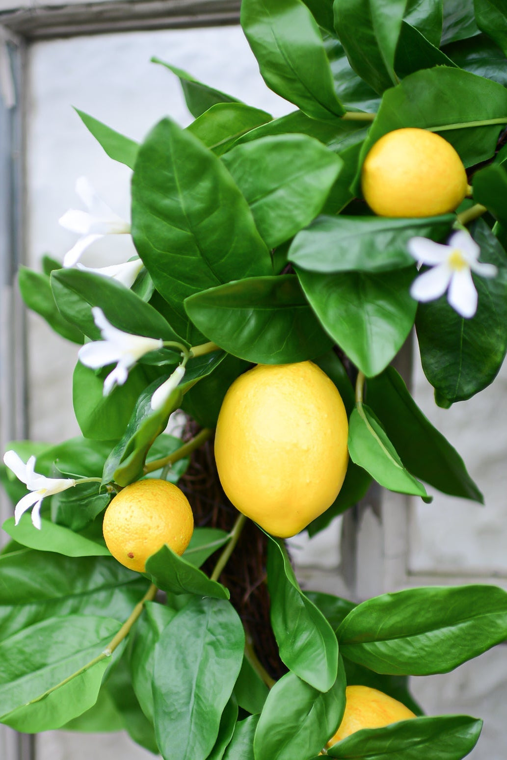 Artificial lemon garland with bright yellow faux lemons, glossy green leaves, and small white flowers, draped in front of a rustic gray paneled door.