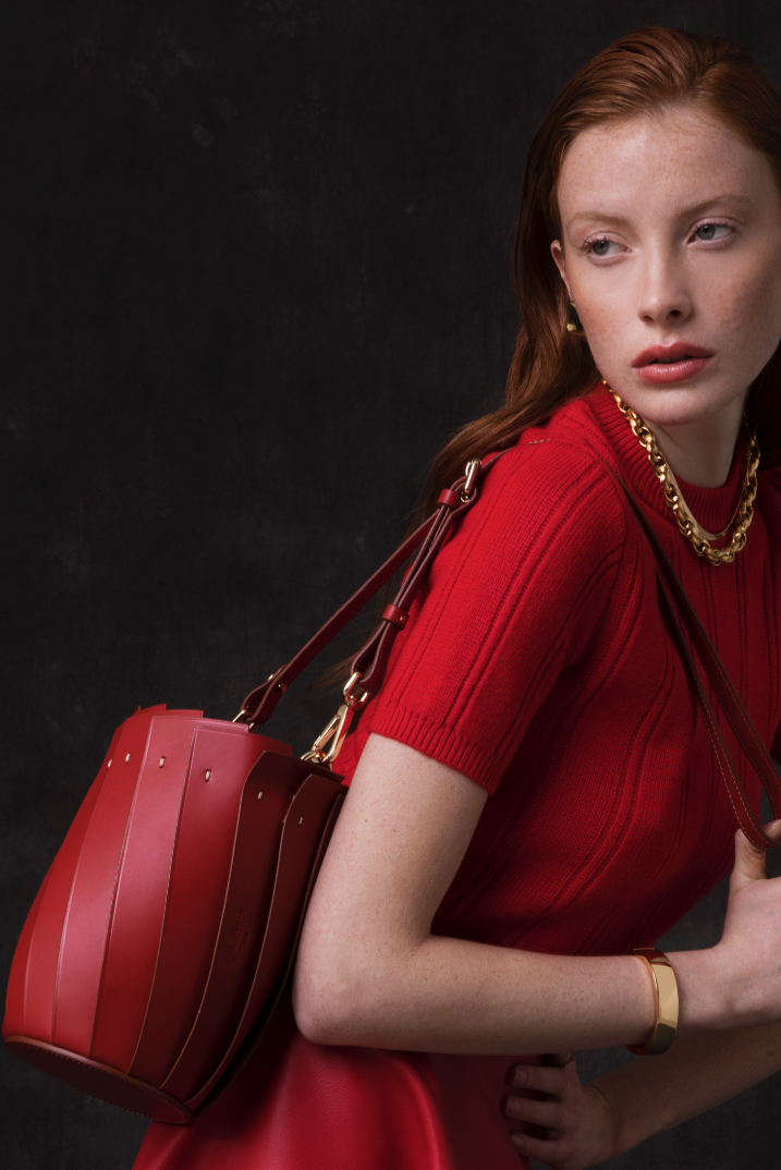 Woman in a red dress holding a red handbag against a dark background