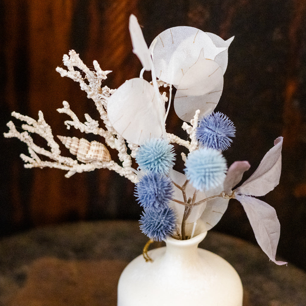 Decorative arrangement with white and blue flowers in a white vase on a dark background