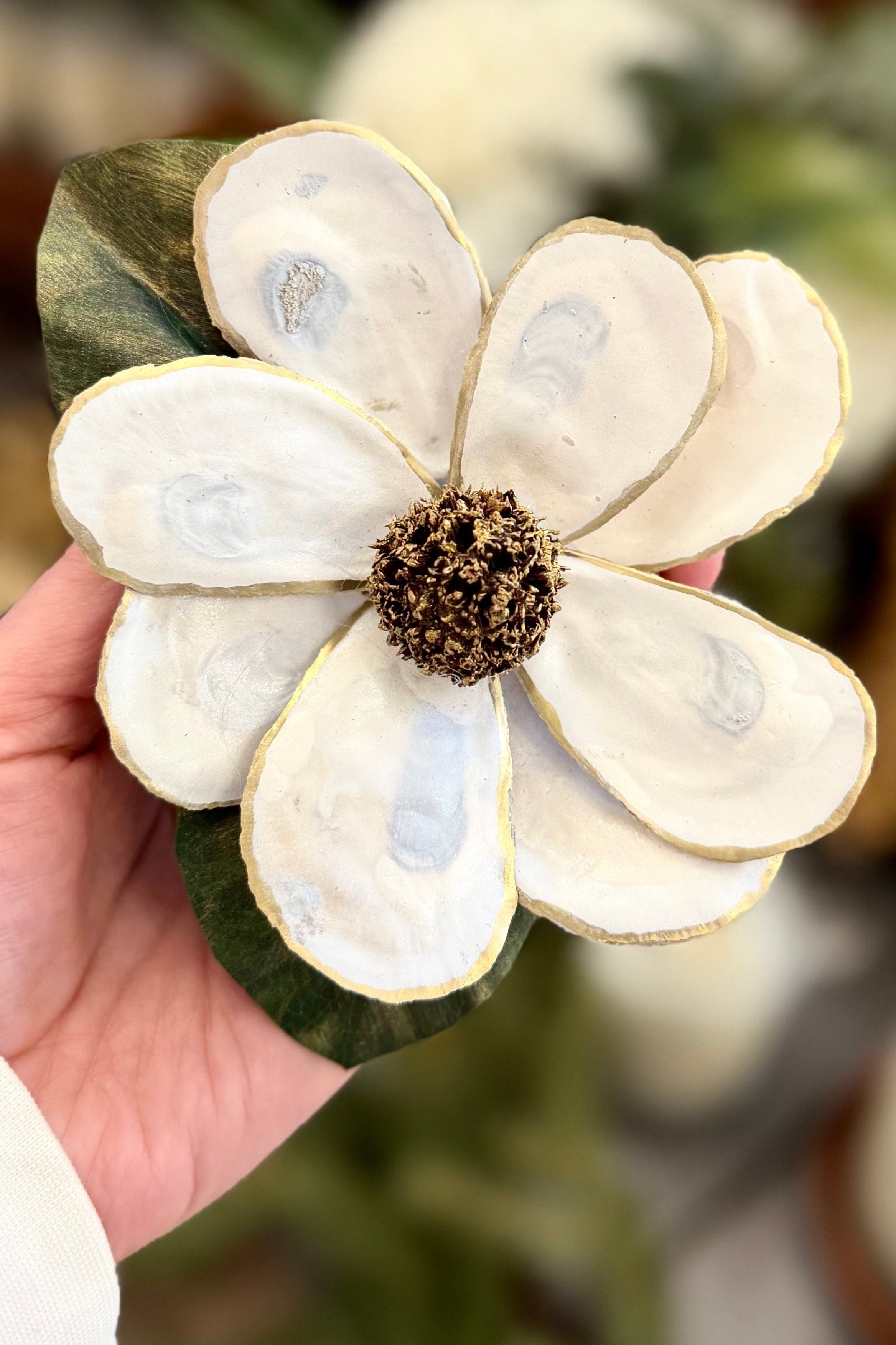 Hand holding a decorative flower with a blurred indoor setting