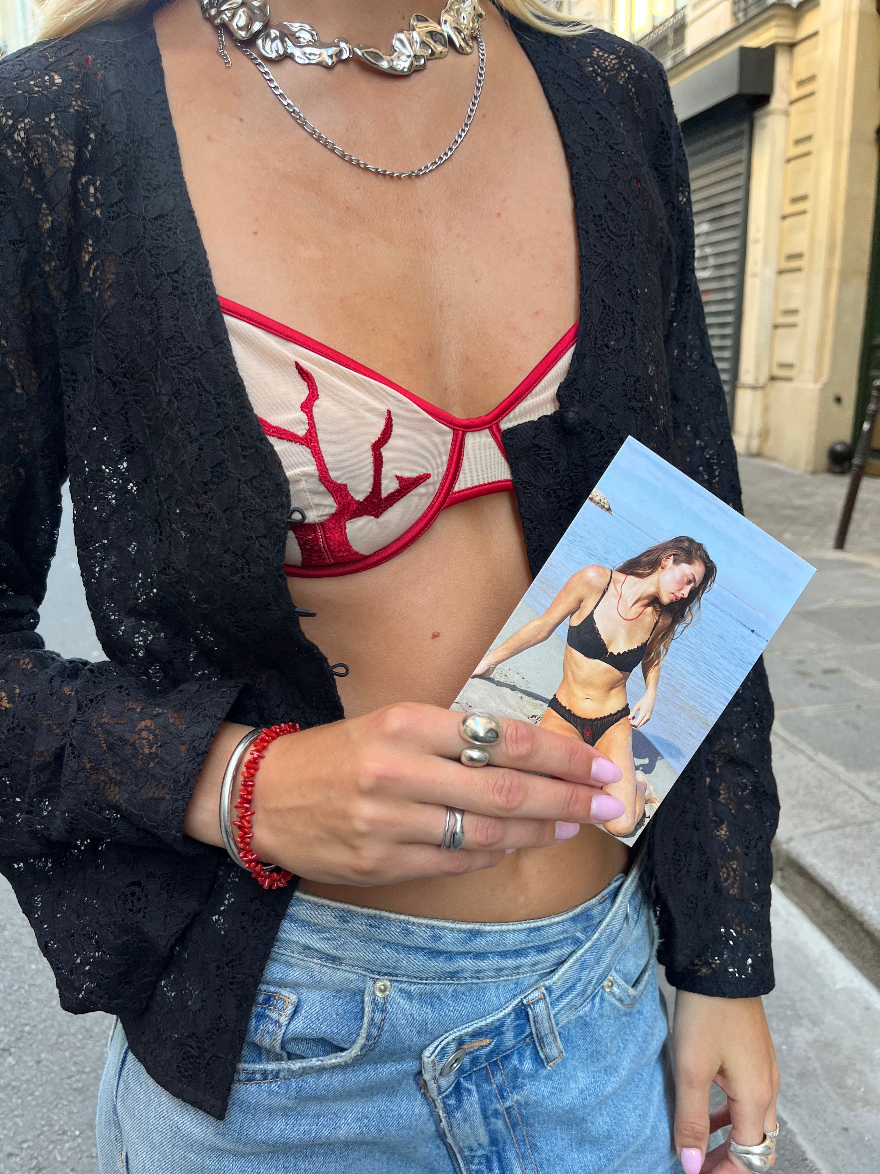 Woman wearing a black lace cardigan with a beige bra with red coral details and a red coral bracelet