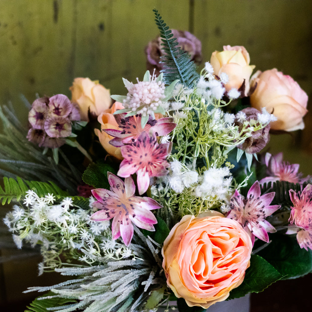 Bouquet of flowers with pink and orange roses, greenery, and white flowers against a blurred background.