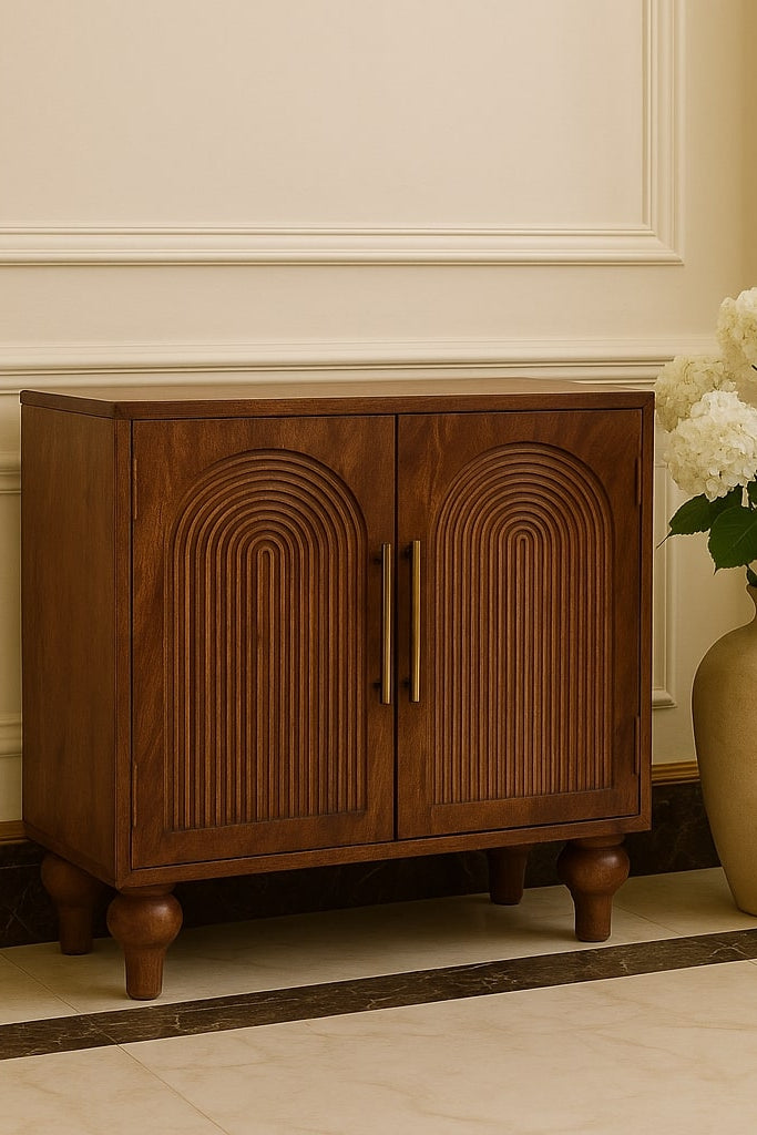Wooden cabinet with decorative arches next to a vase with white flowers on a beige floor.