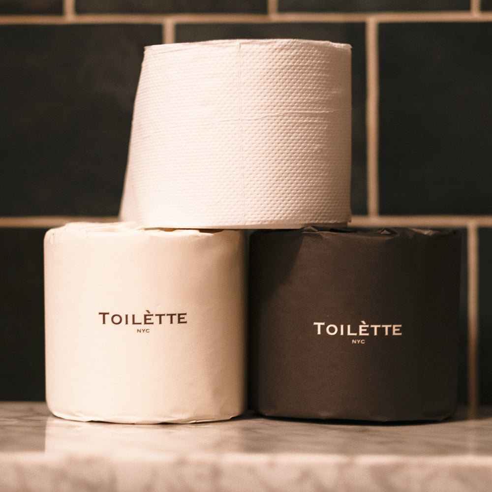 Two rolls of toilet paper with 'TOILETTE NYC' branding on a tiled bathroom wall background.