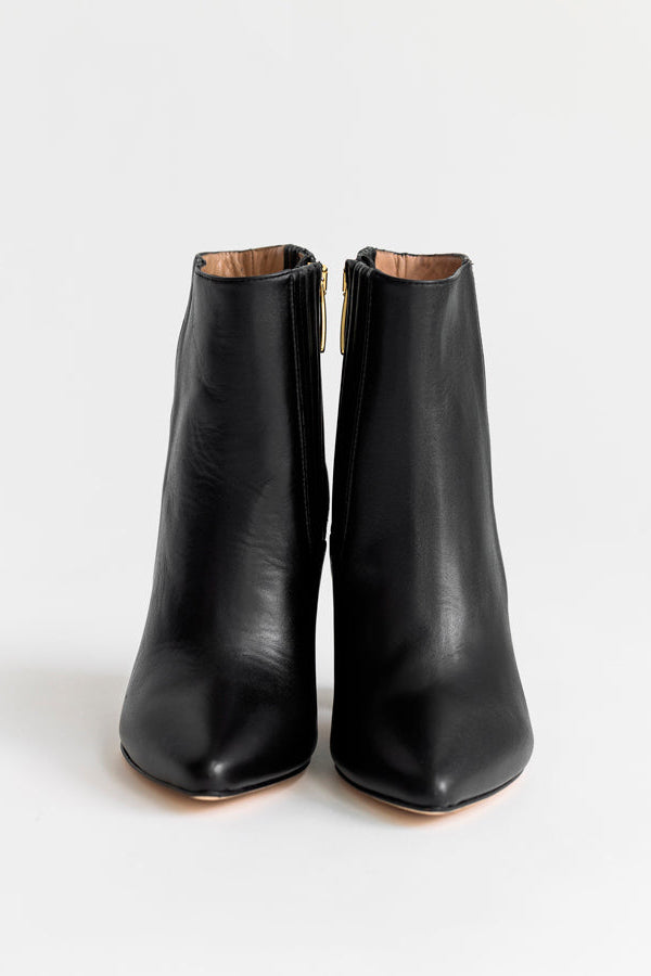 A pair of black leather ankle boots with a pointed toe and a small gold-tone zipper pull, shown from the front on a light gray background.