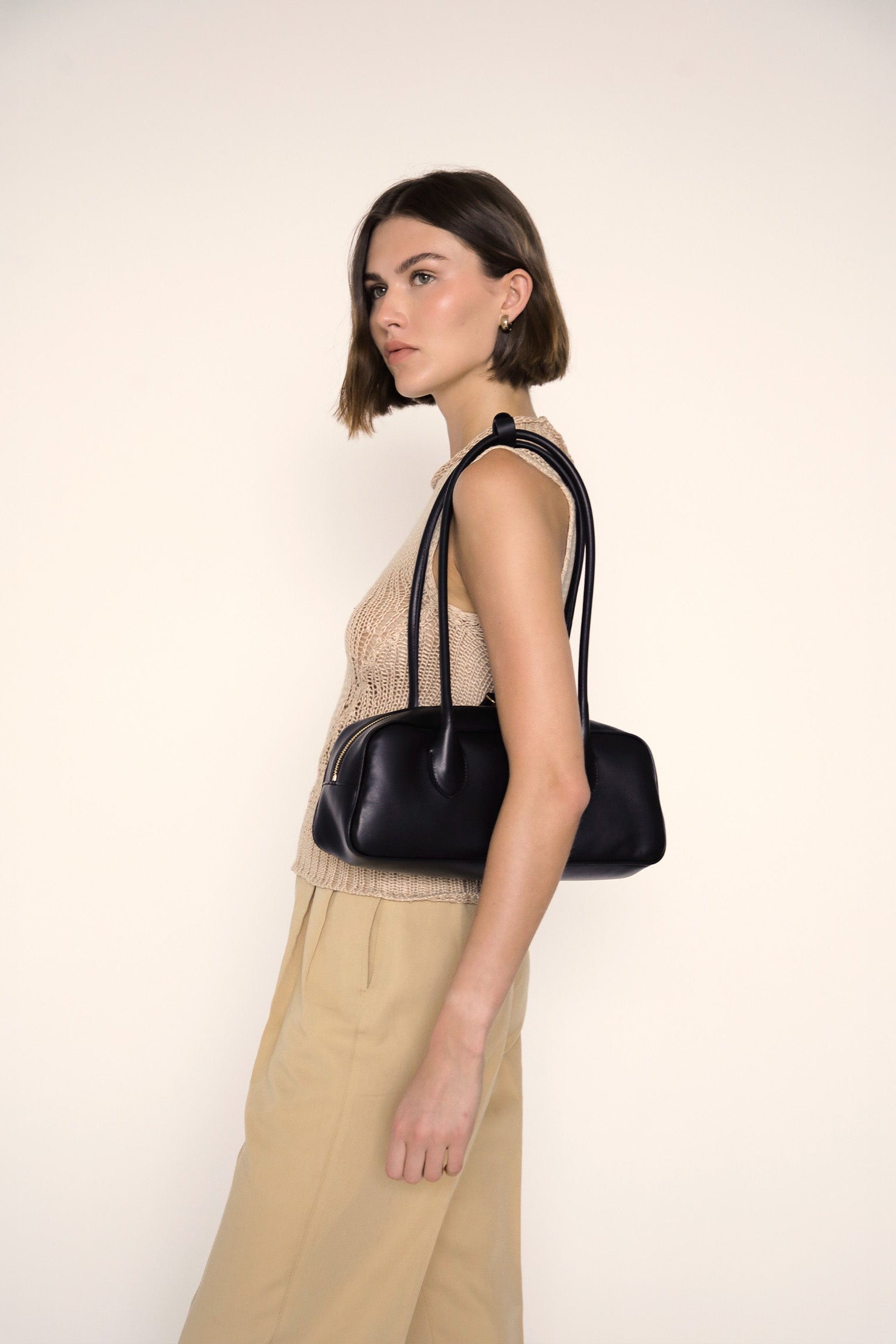 Woman holding a black handbag against a plain background