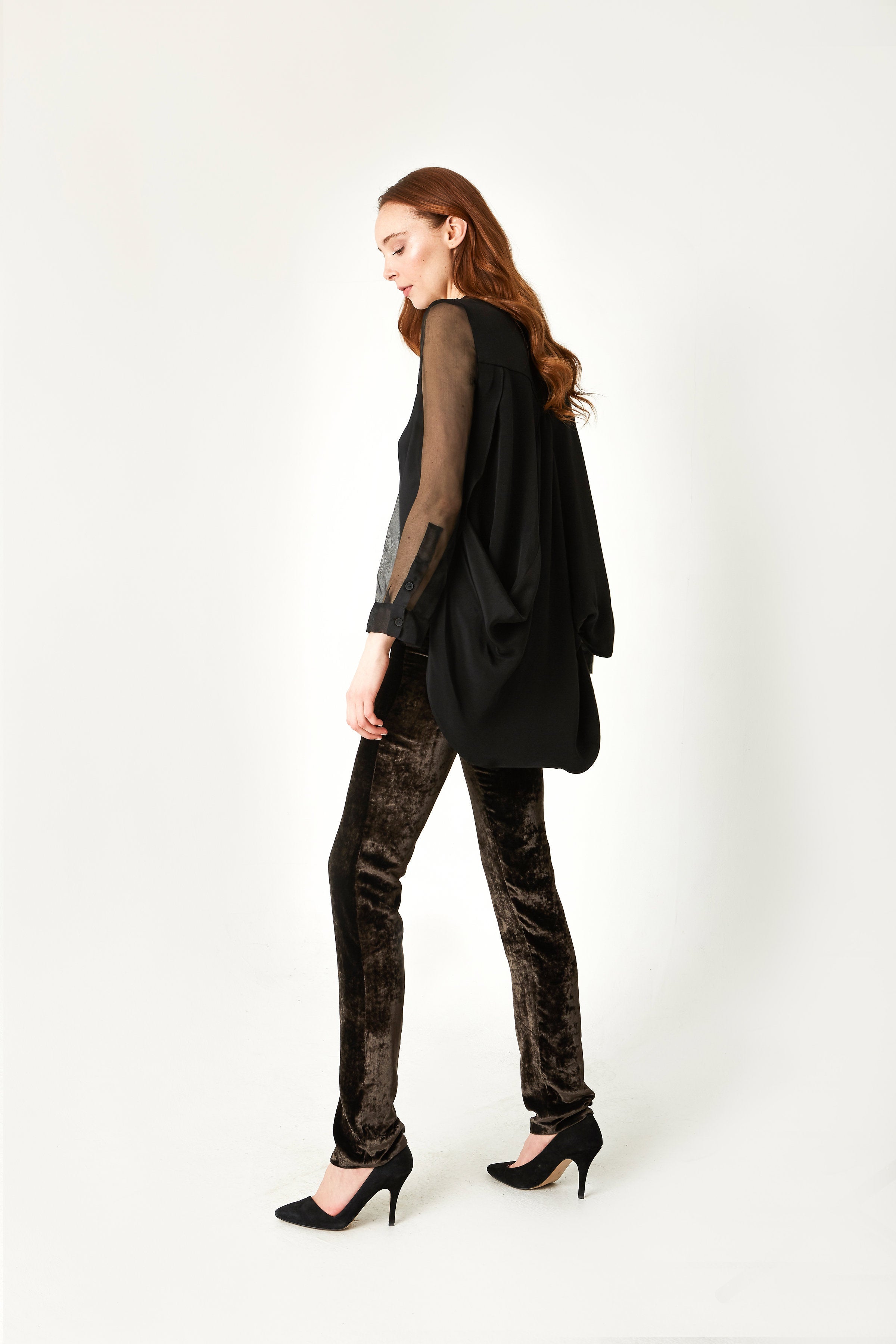 Woman wearing a black outfit with a silk sheer top and patterned pants on a white background