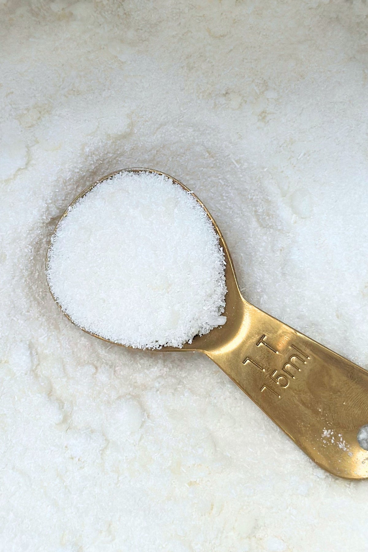 Brass measuring spoon filled with white powder on a marble surface