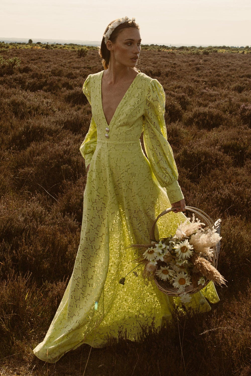 Woman in a long yellow dress holding a basket of flowers in a field.